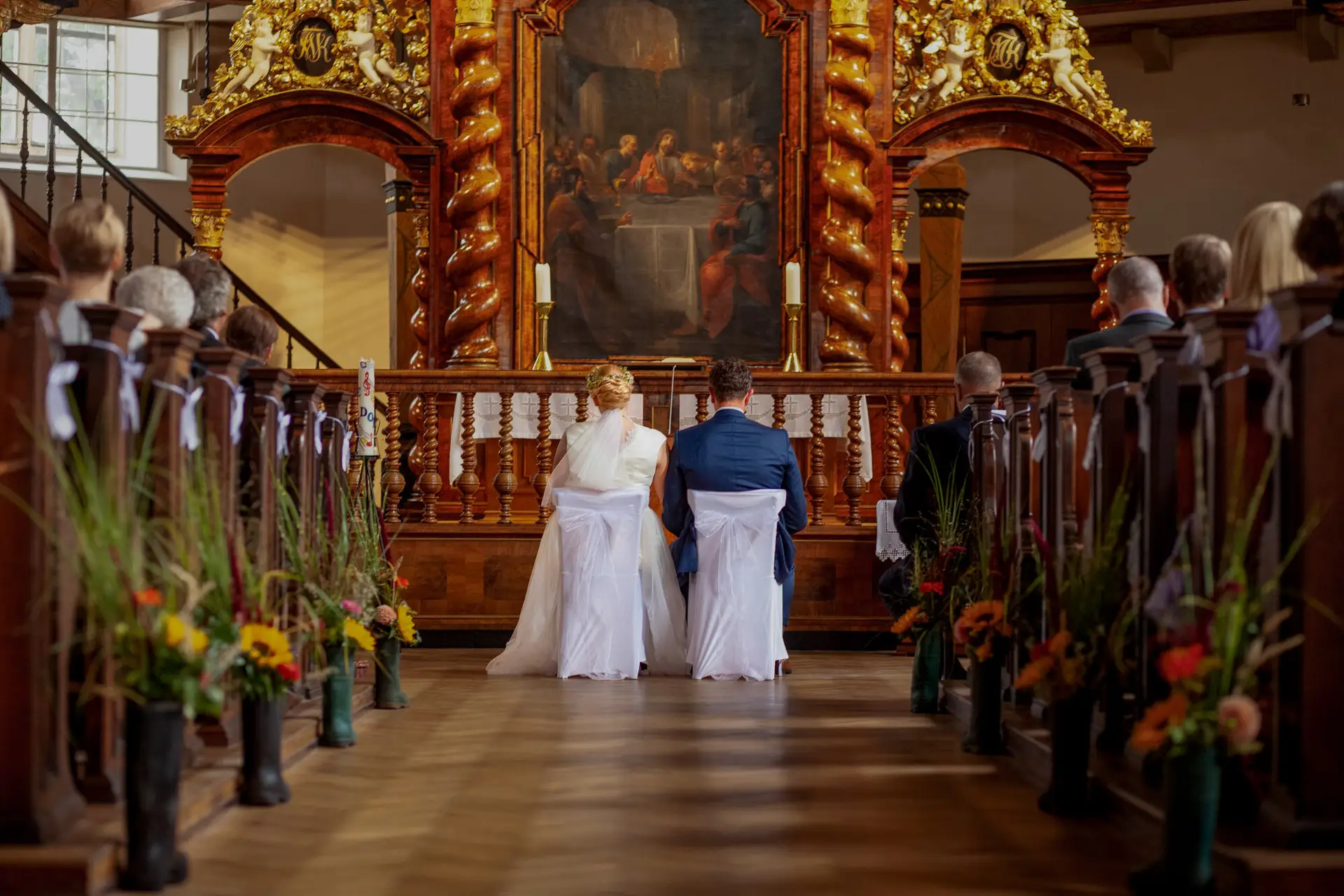 20180915 13 47 58 20180915 13 47 58 Geng Rummer Speyer Reilingen IMG 2042 Weiss Hochzeit Kirchenaltar Stuhls Hochzeitsfotograf Reilingen Speyer Ida Philipp.67m19c84 Brautpaar kniet am Altar einer Kirche mit Blumendekoration und Kirchenfenstern