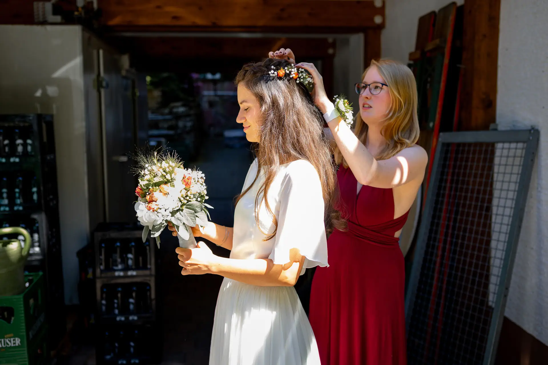 20230811 14 26 04 Hochzeit Elztal Hochzeitsfotograf Heiraten Heidelberg Landgasthof Heidersbacher Muehle 4K8A0830.JQKSwh J Braut mit Blumenkrone am Haar, Brautjungfer hilft bei letzten Vorbereitungen vor der Trauung