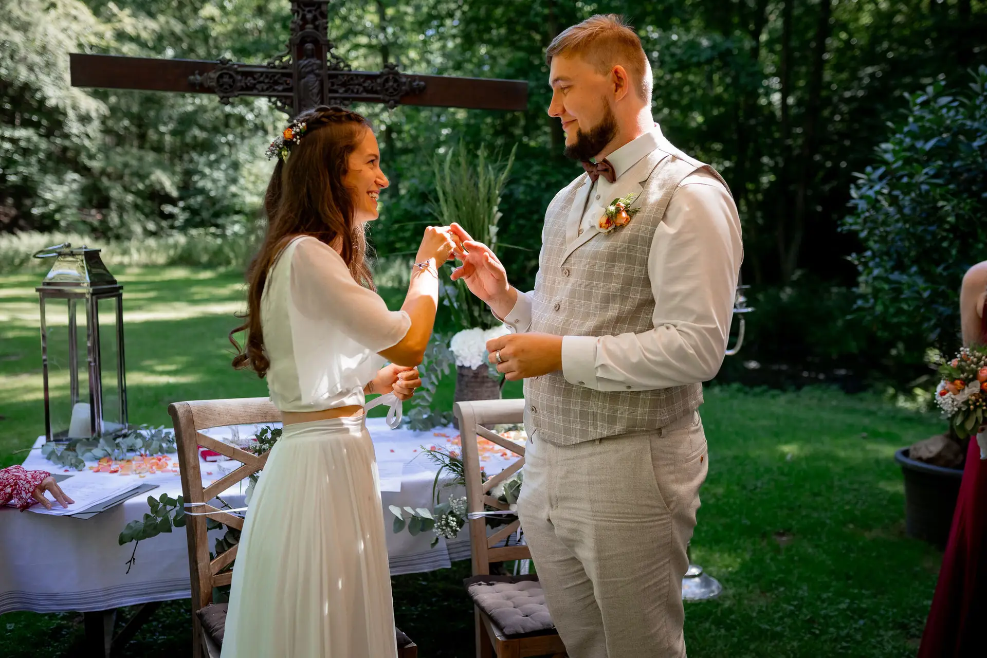 20230811 15 00 05 Hochzeit Elztal Hochzeitsfotograf Heiraten Heidelberg Landgasthof Heidersbacher Muehle 4K8A1826.BaWhvb2z Brautpaar reicht sich gegenseitig eine Kette vor dem Holzkreuz – persönliches Zeremonieritual der beiden