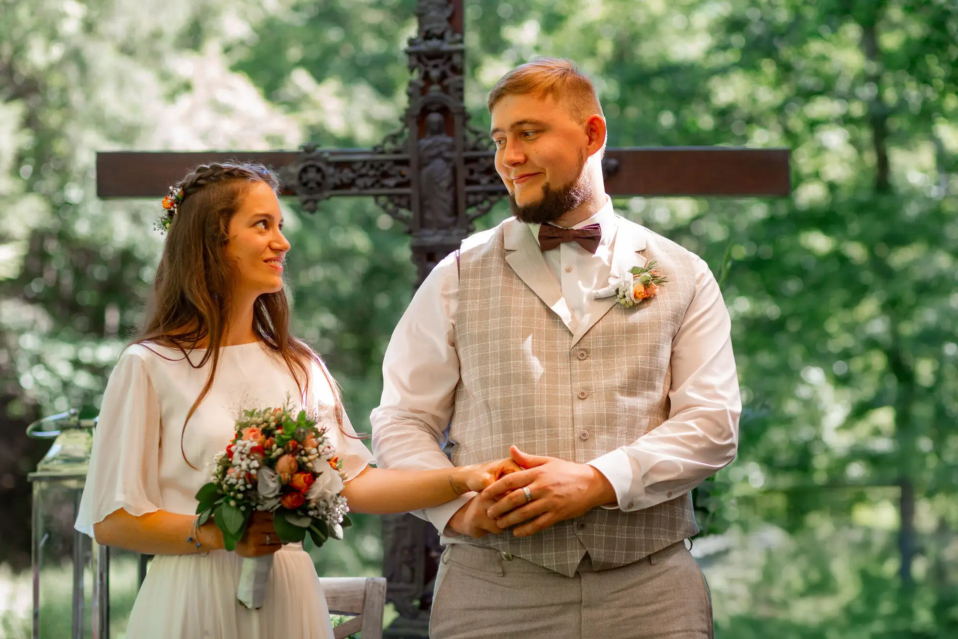 20230811 15 01 26 Hochzeit Elztal Hochzeitsfotograf Heiraten Heidelberg Landgasthof Heidersbacher Muehle MK3 9260.DPM6n7sq Brautpaar blickt sich zärtlich an vor dem verzierten Metallkreuz – stiller Moment nach der Trauung