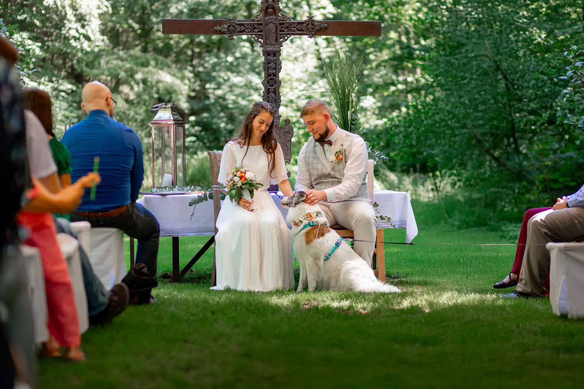 20230811 15 05 56 Hochzeit Elztal Hochzeitsfotograf Heiraten Heidelberg Landgasthof Heidersbacher Muehle MK3 9383.BlllEMax Braut und Bräutigam sitzen auf Bank mit der weißen Hündin, Gäste gratulieren im Hintergrund