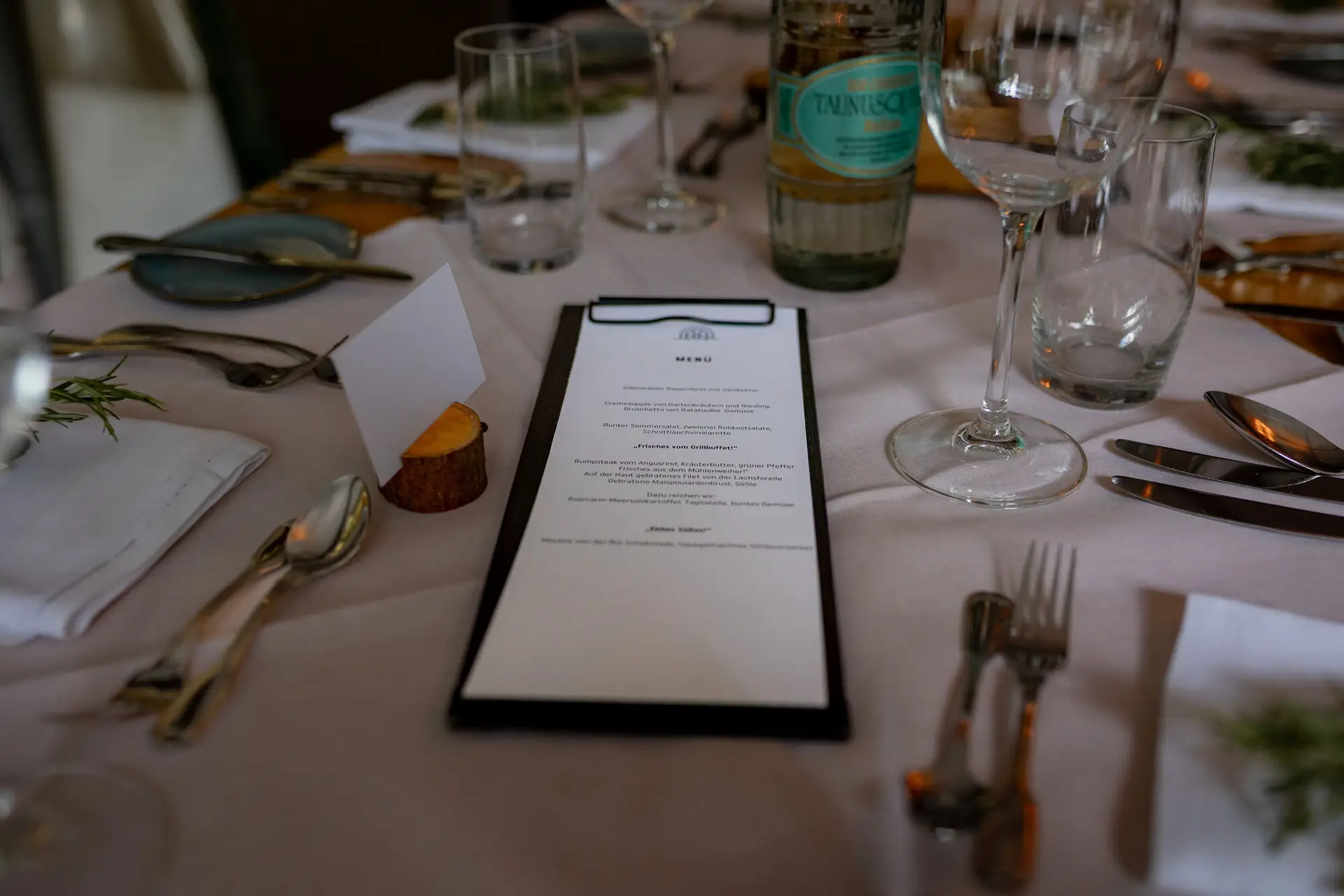 20230811 18 40 11 Hochzeit Elztal Hochzeitsfotograf Heiraten Heidelberg Landgasthof Heidersbacher Muehle 4K8A7260.DZ3E4r5x Tischdetail des Hochzeitsabendessens: Menükarte, Weinflasche und persönliche Dekoration