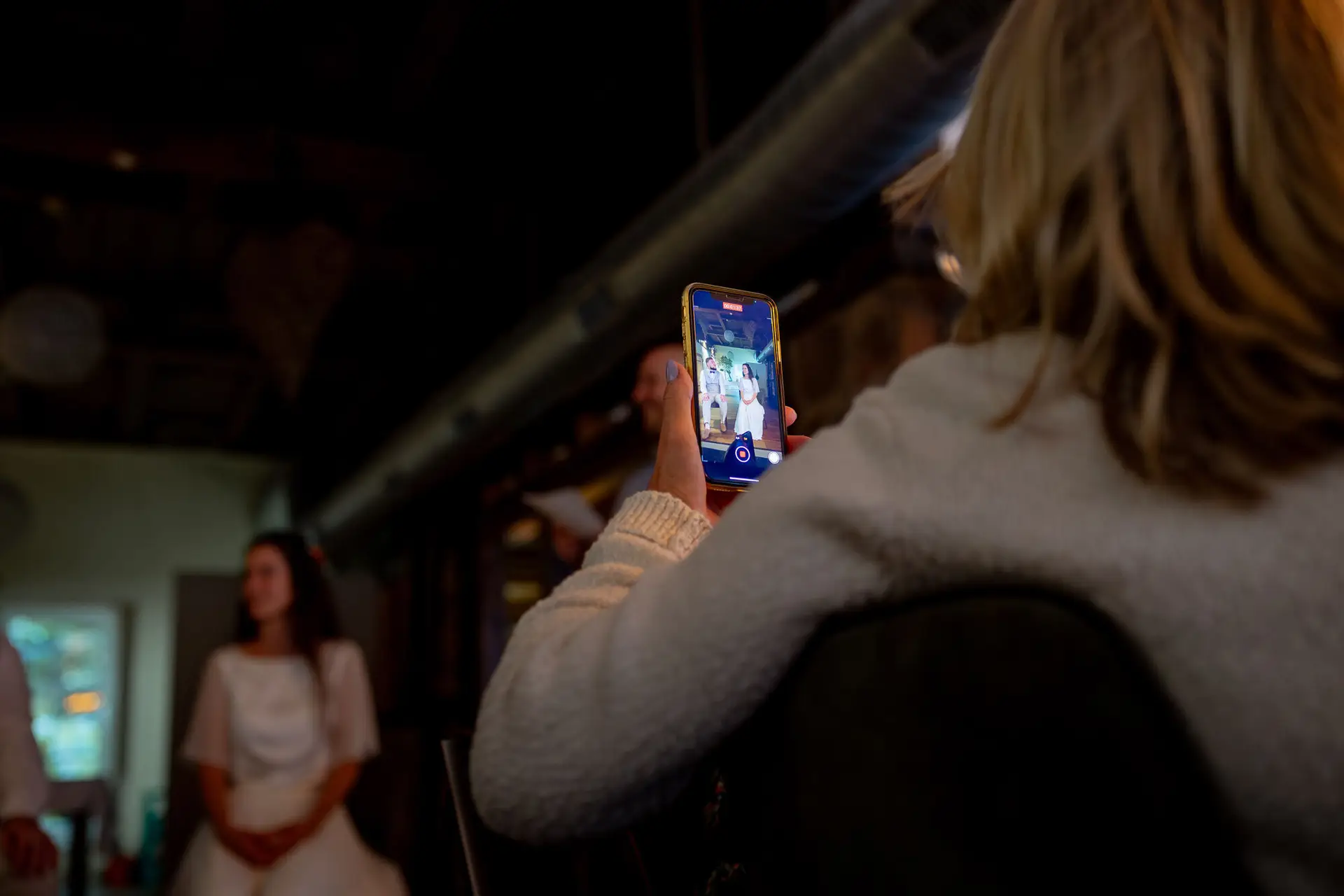 20230811 20 20 13 Hochzeit Elztal Hochzeitsfotograf Heiraten Heidelberg Landgasthof Heidersbacher Muehle 4K8A7478 Verbessert RR.D4Kk46iT Gast filmt mit Smartphone einen besonderen Moment beim Abendessen – die Braut im Fokus