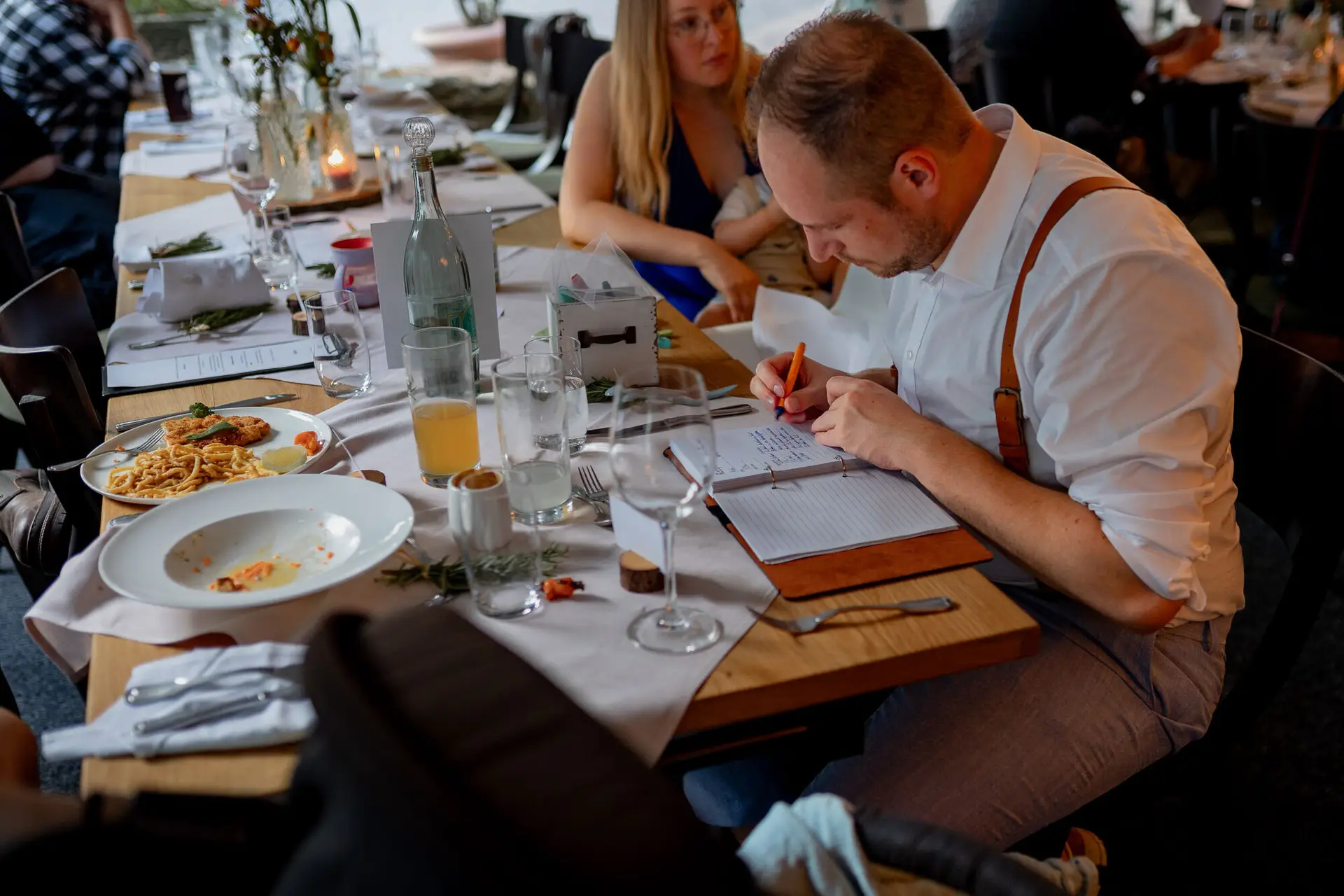 20230811 20 26 12 Hochzeit Elztal Hochzeitsfotograf Heiraten Heidelberg Landgasthof Heidersbacher Muehle 4K8A7651.BAFtMv14 Hochzeitsspiel beim Abendessen: Gast schreibt ins Notizbuch bei Pasta und Wein