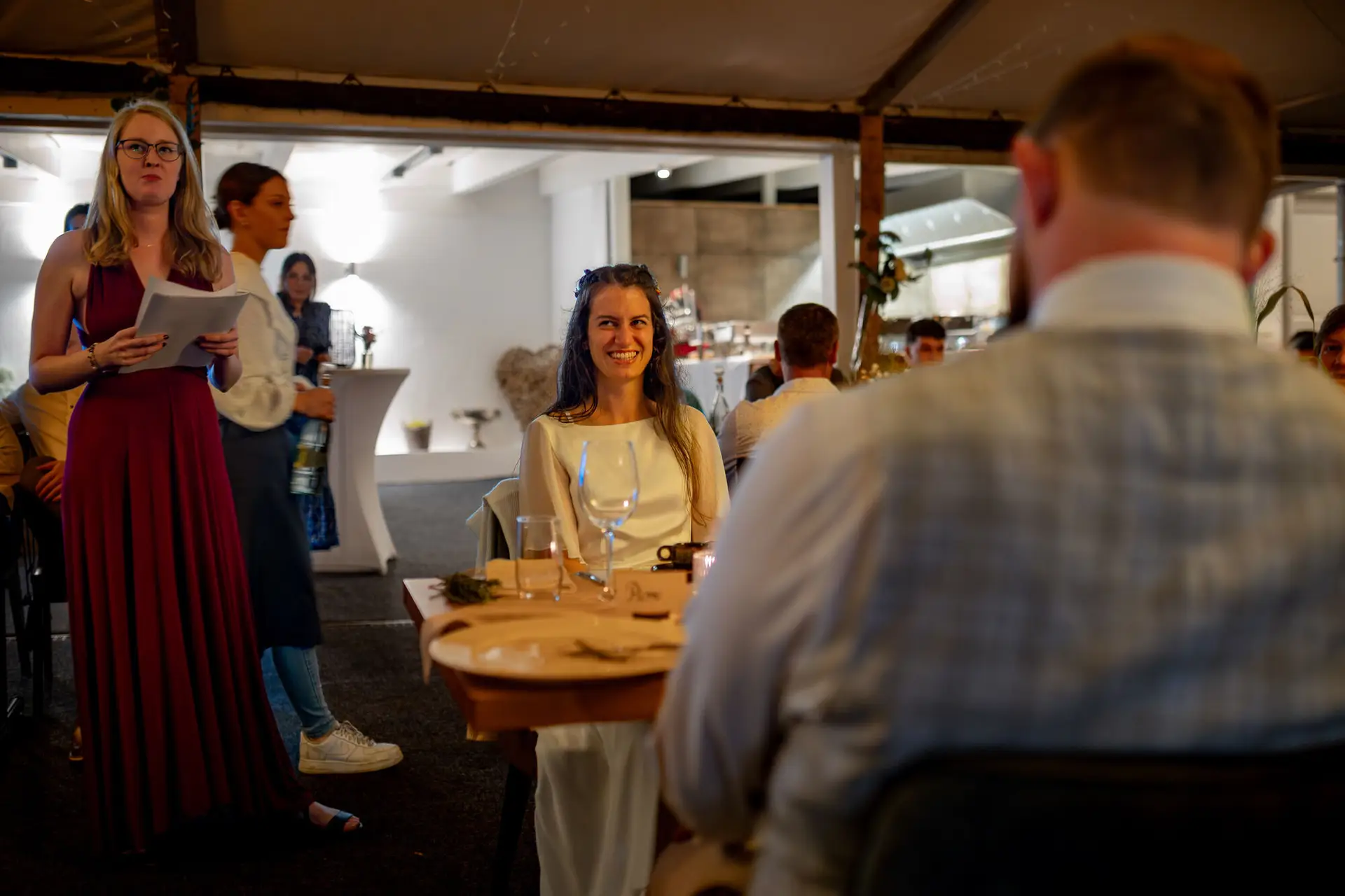 20230811 21 40 11 Hochzeit Elztal Hochzeitsfotograf Heiraten Heidelberg Landgasthof Heidersbacher Muehle 4K8A9102 Verbessert RR.DhZiYE8M Braut lächelt glücklich in die Kamera beim Hochzeitsabend, Bräutigam schaut aus dem Hintergrund