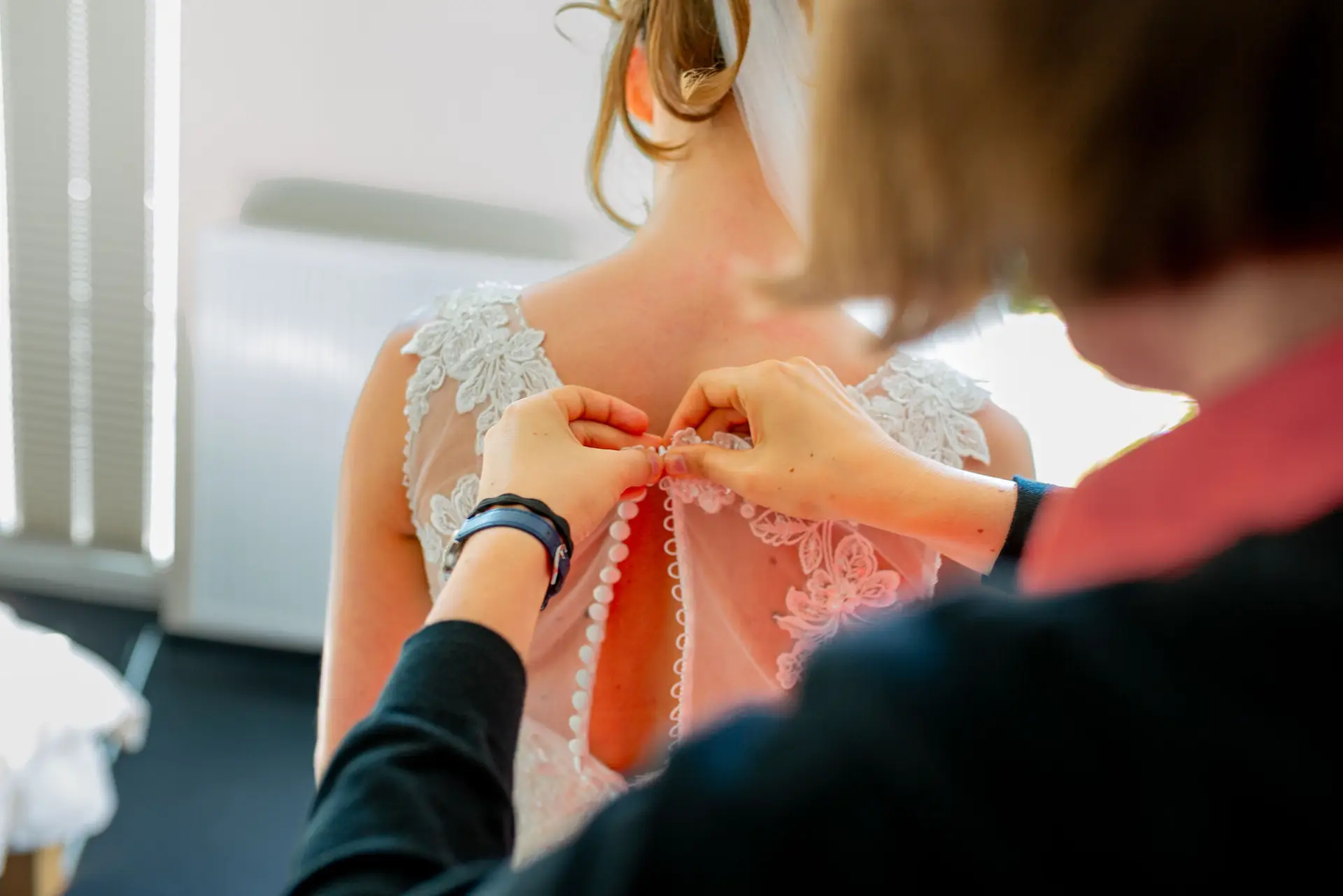 Anne Christian Hochzeitsfotograf Birkenheide Grosskarlbach Bissersheim 00002.JIC47Vjo Hand befestigt zart weiße Perlen am Rücken des hochgesteckten, blumengeschmückten Brautkleides