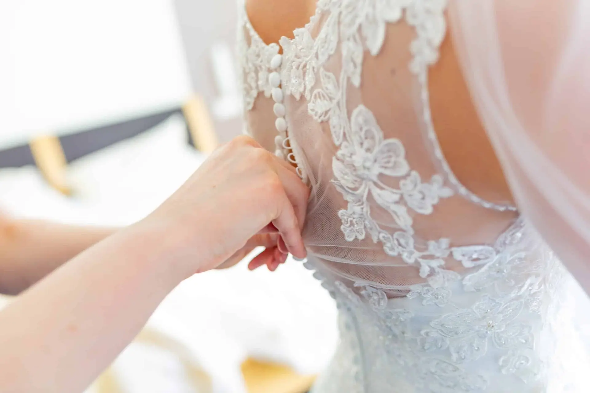 Anne Christian Hochzeitsfotograf Birkenheide Grosskarlbach Bissersheim 16.D1NE68MU Nahaufnahme der Hand, die feines Spitzendetail am Rücken der Braut im hochgeschlossenen weißen Hochzeitskleid formt