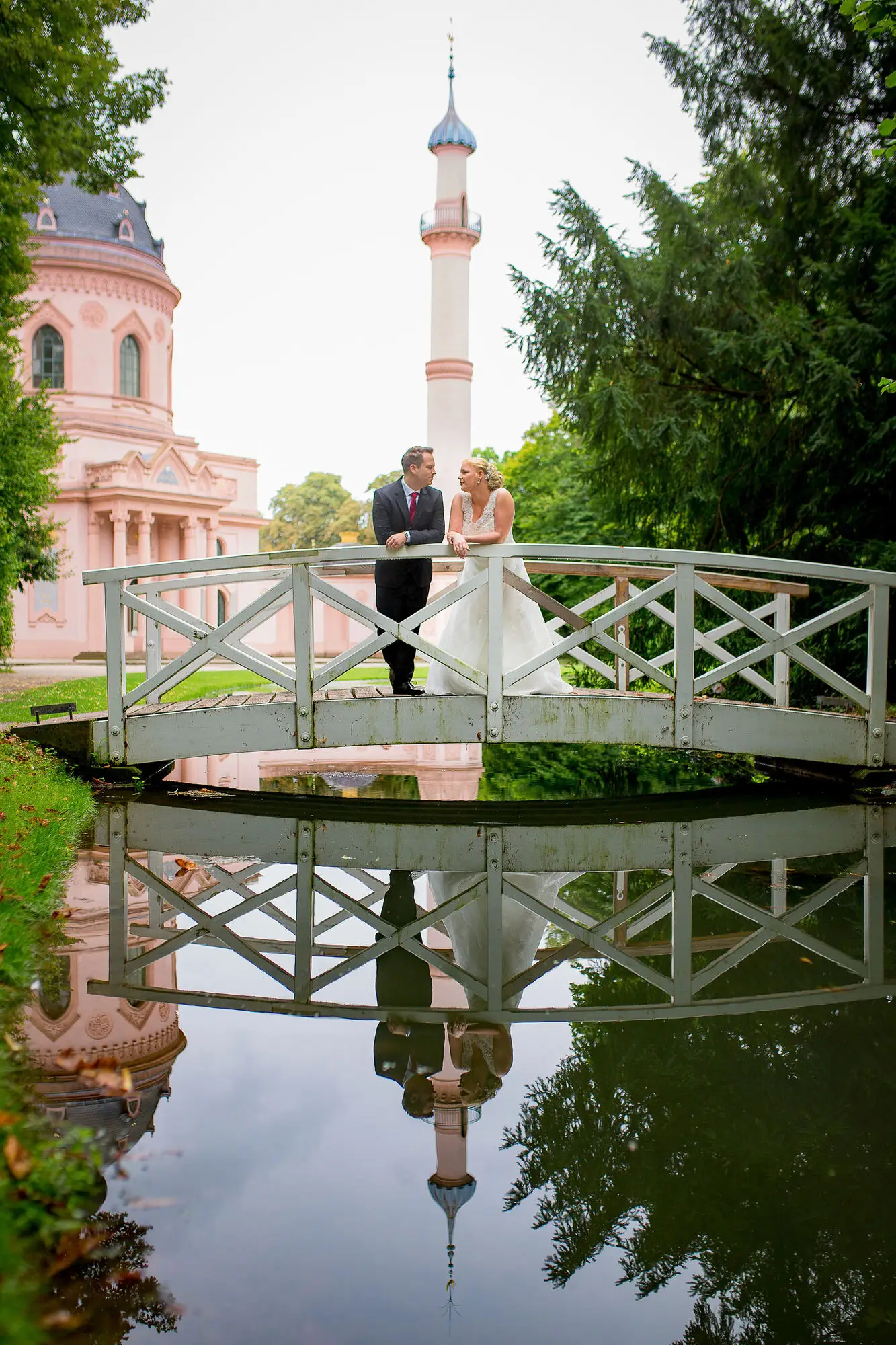 Cindy Dominik Schwetzingen Bruecke Minarett.Qadtu7Dt Brautpaar auf einer weißen Brücke über dem Schlossteich, Spiegelung des maurischen Minarett-Turms im Wasser