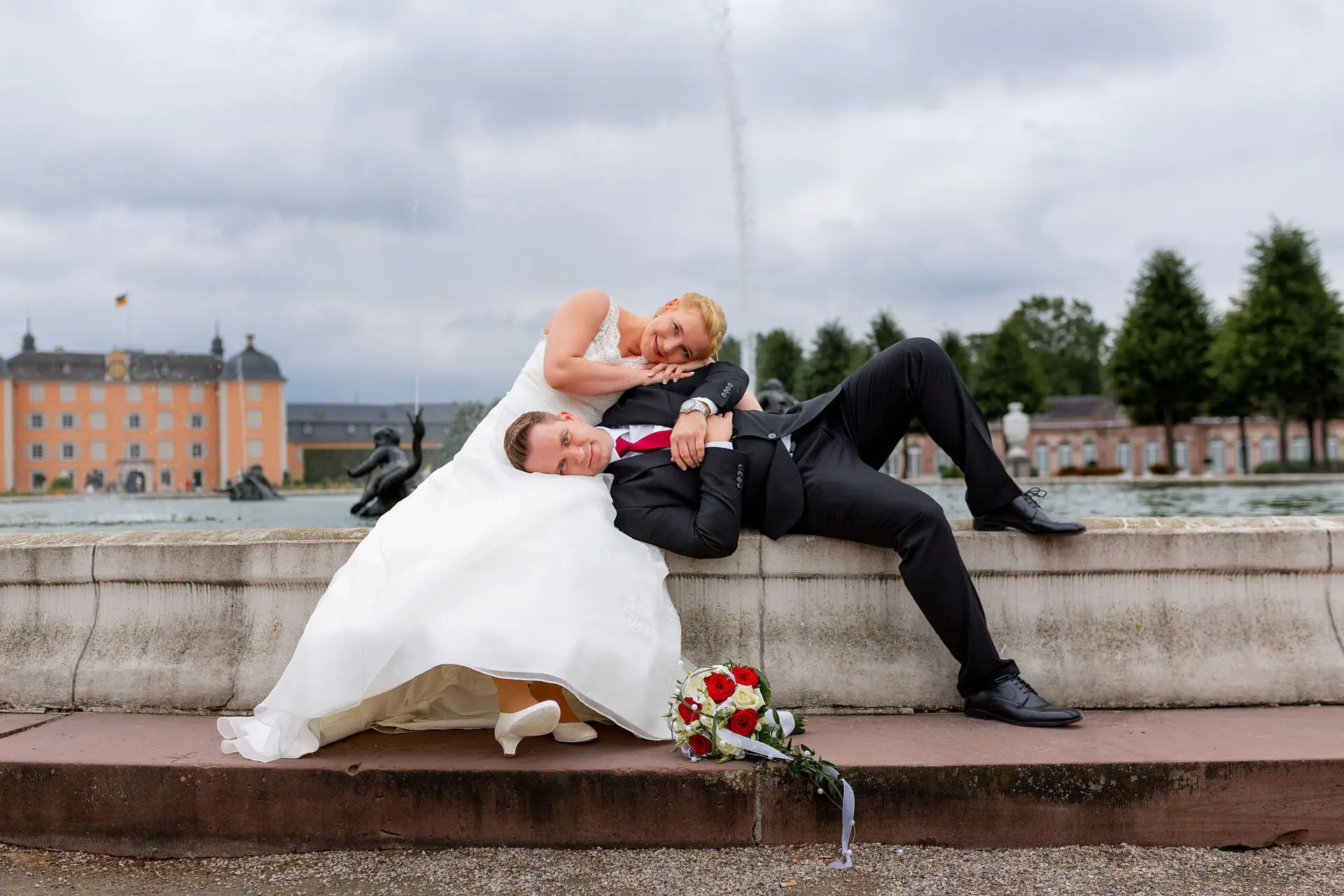 Cindy Dominik Schwetzingen Brunnenrand Fontaene.Ype0Z4Hf Brautpaar liegt entspannt am Brunnenrand, Schloss Schwetzingen und Fontäne im Hintergrund