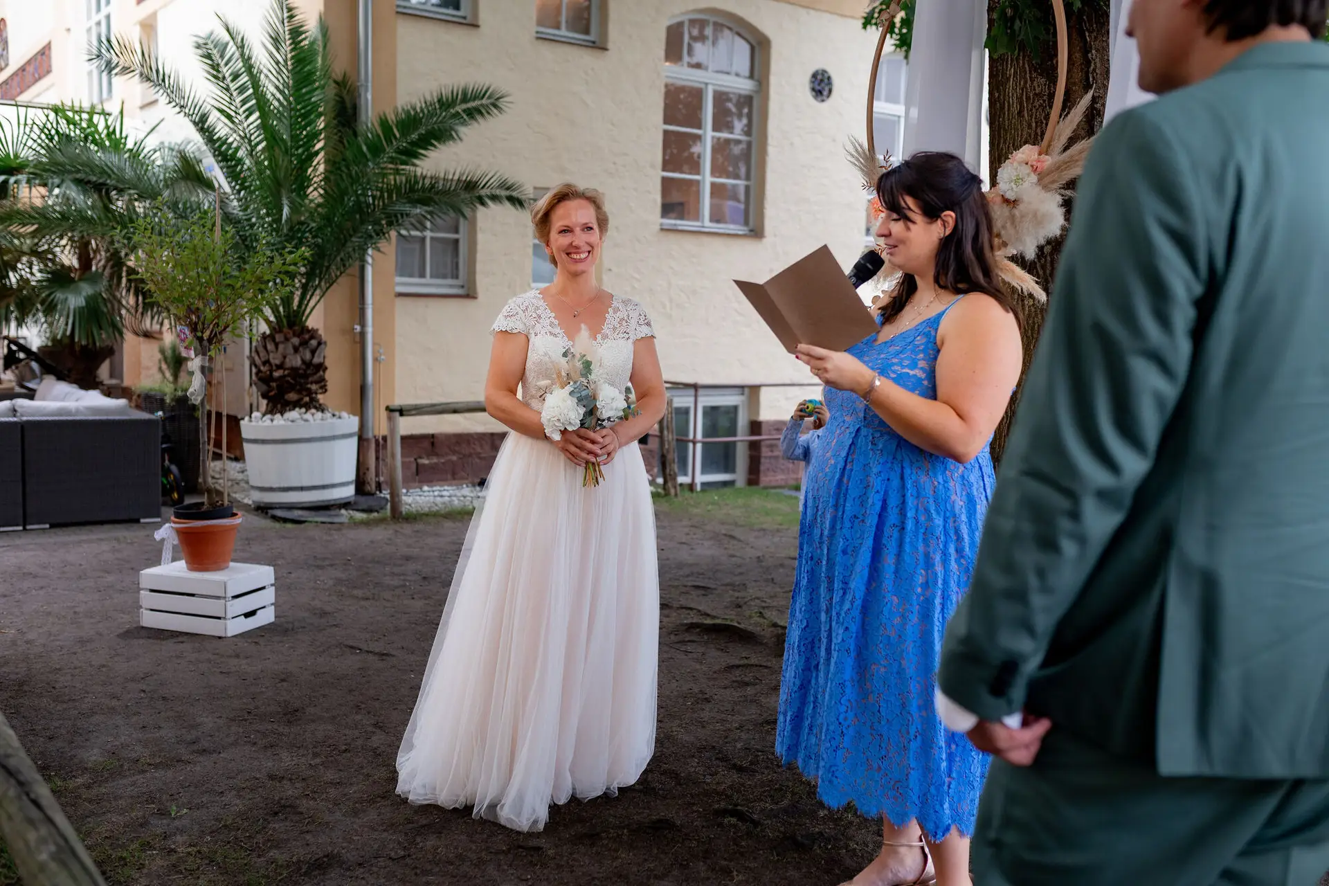 Daniela Matthias Cantina Traurednerin Braut Strahlt.DQRtxfT5 Traurednerin liest aus der Mappe bei der freien Trauung, Braut strahlt mit Brautstrauß
