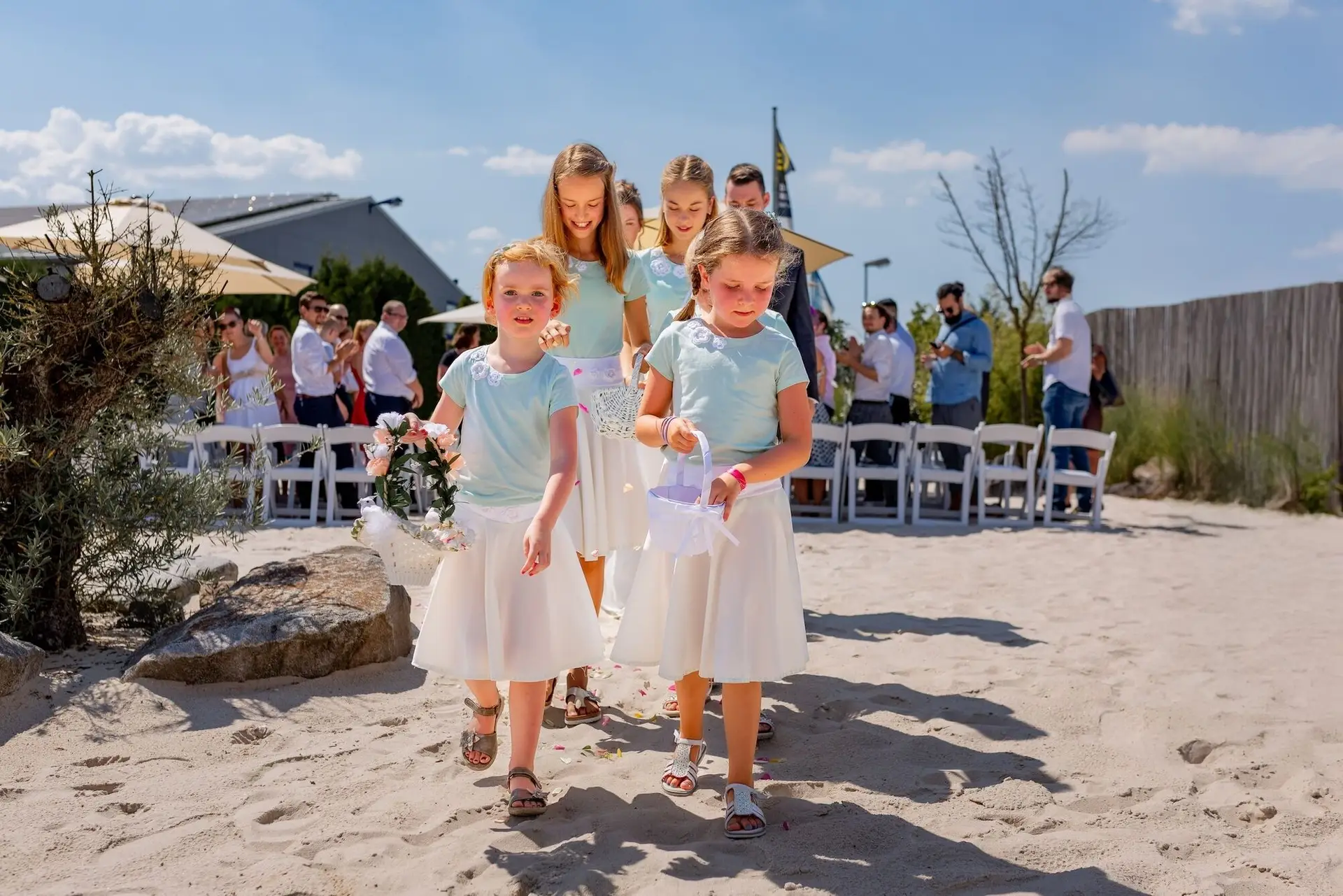 Blumenmädchen in hellblauen Kleidern streuen Blütenblätter auf dem Weg zum Altar auf dem Sandstrand