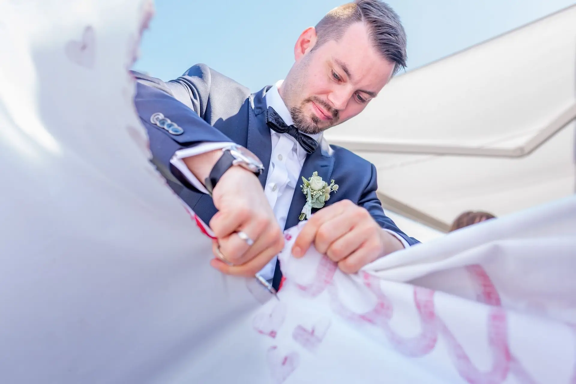Bräutigam schreibt mit rotem Stift auf das große florales Hochzeitsbanner – persönliche Erinnerung für das Paar
