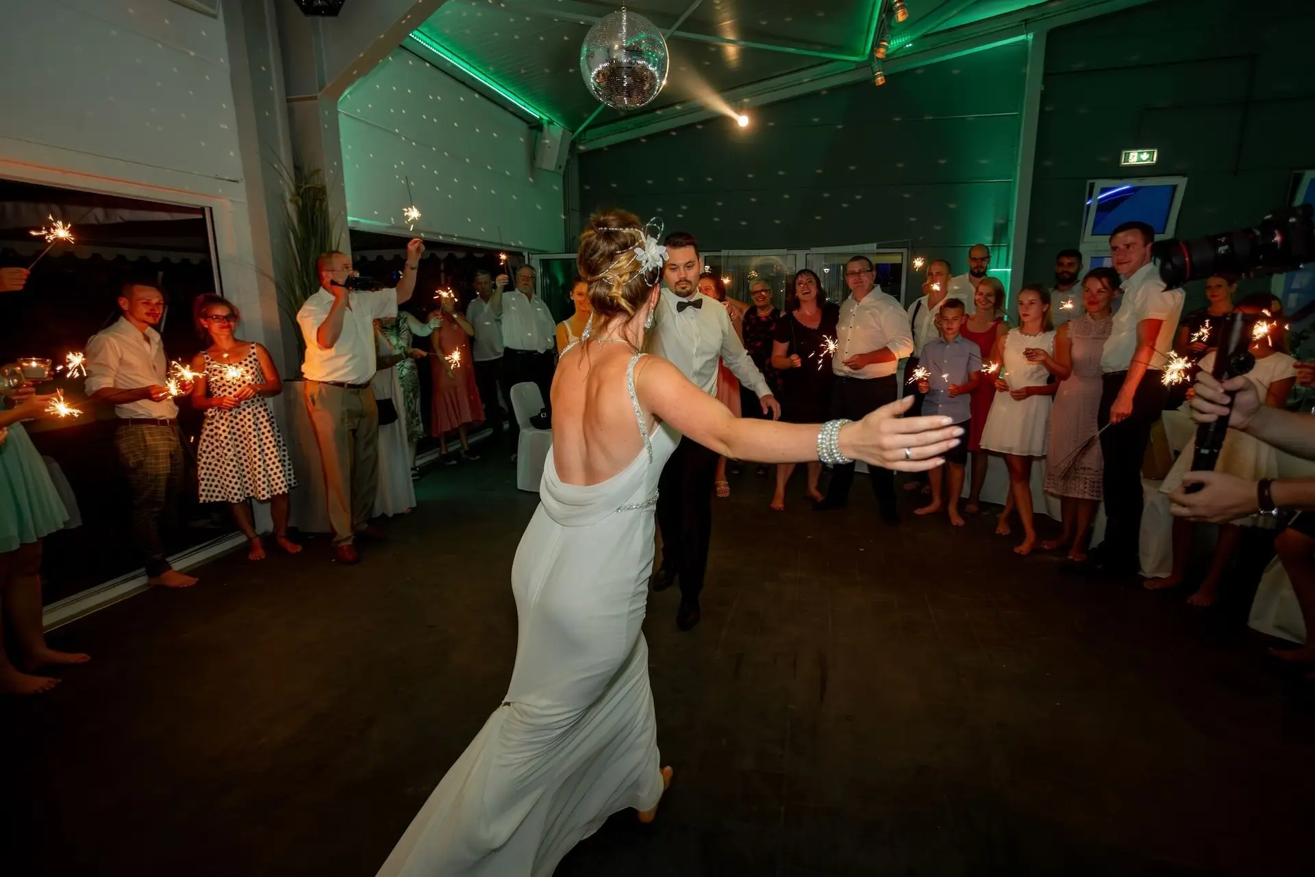 Brautpaar tanzt in der Mitte der jubelnden Gäste mit Wunderkerzen, Discoball und grünem Partylicht