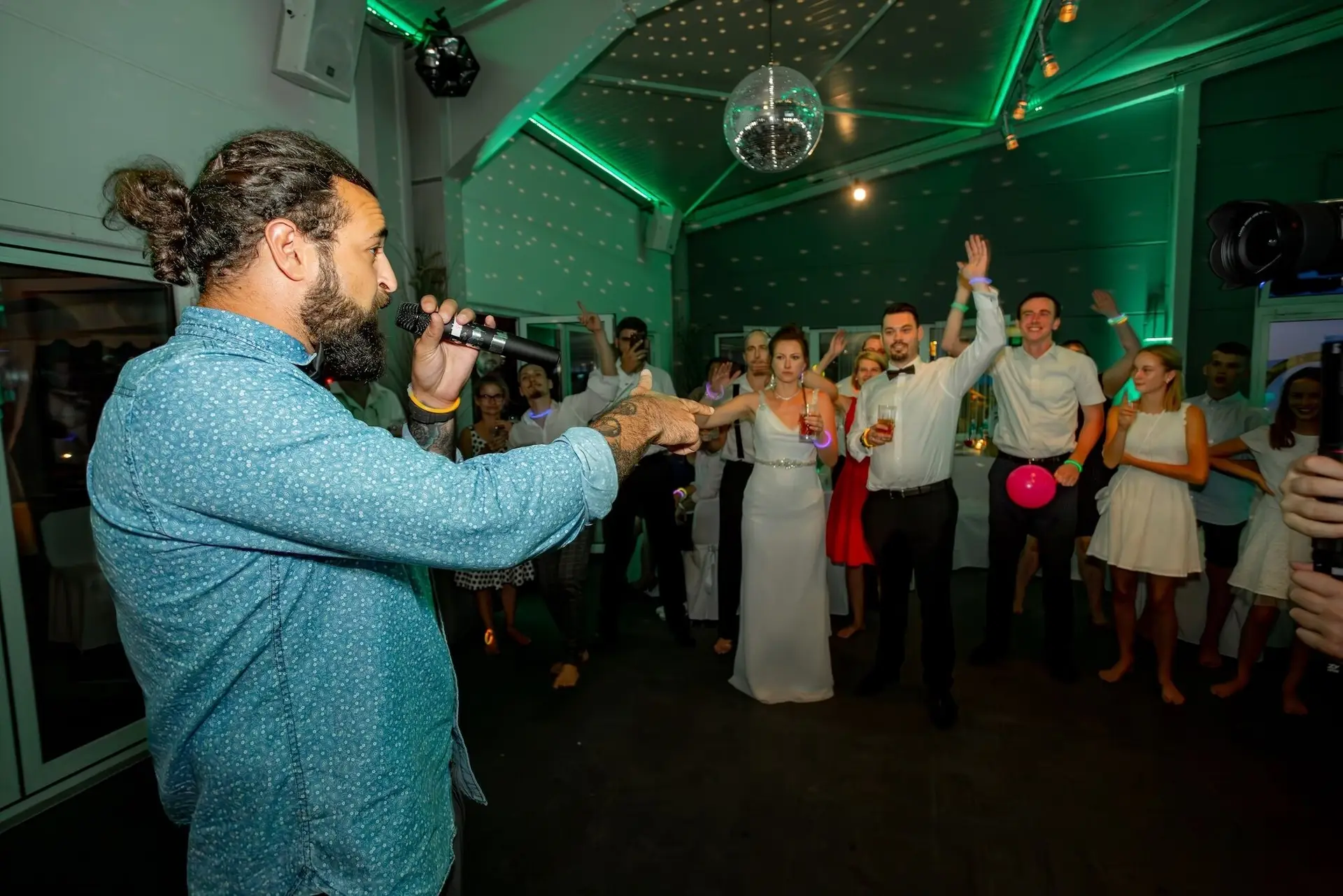 DJ und Moderator animiert die Tanzfläche, Brautpaar tanzt begeistert mit den Gästen unter dem Discoball
