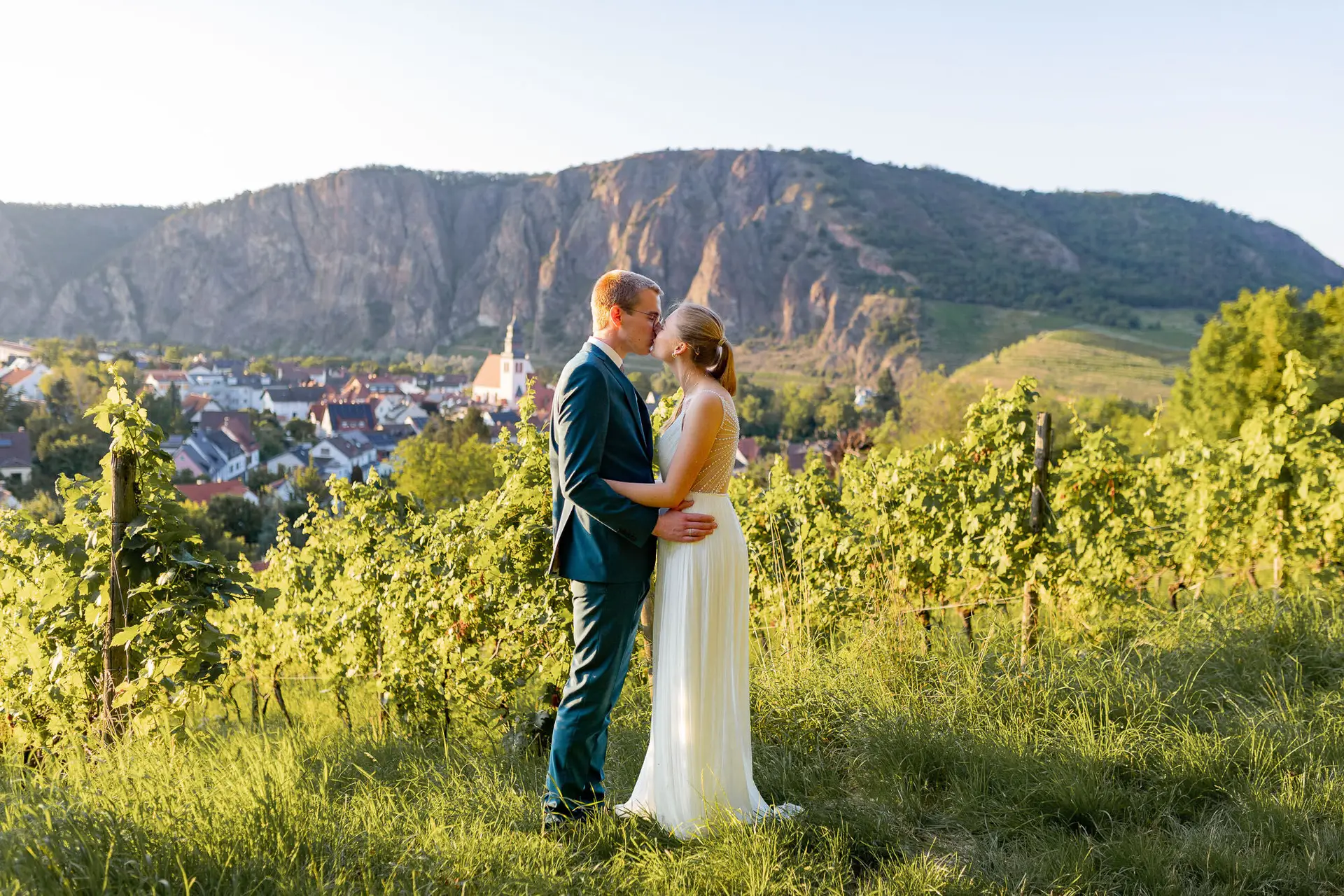 Brautpaar küsst sich mit Blick auf Weinberge und die Burg Ebernburg in der Abenddämmerung