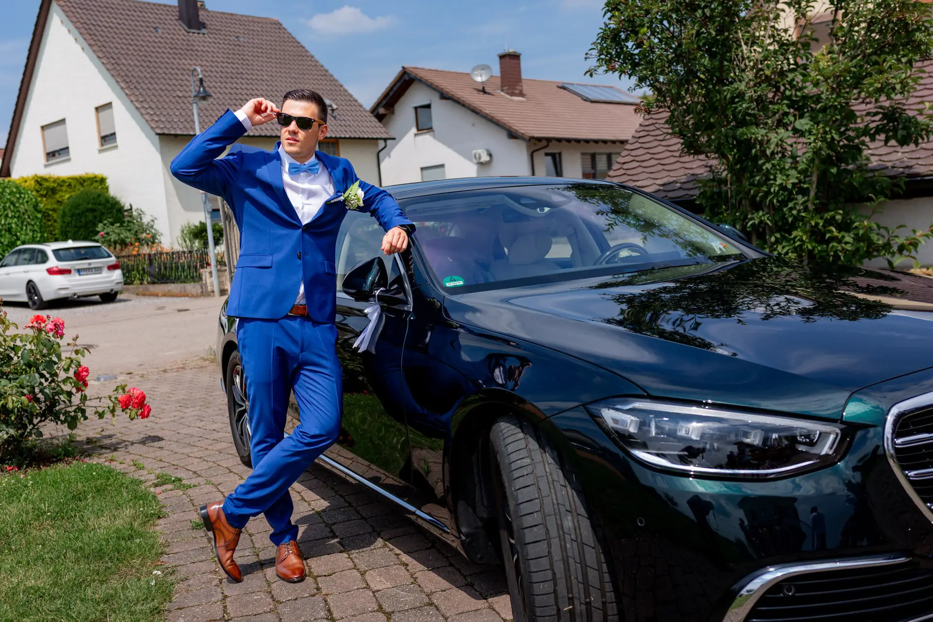 Bräutigam Kevin posiert lässig mit Sonnenbrille am Hochzeitsauto nach der Trauung