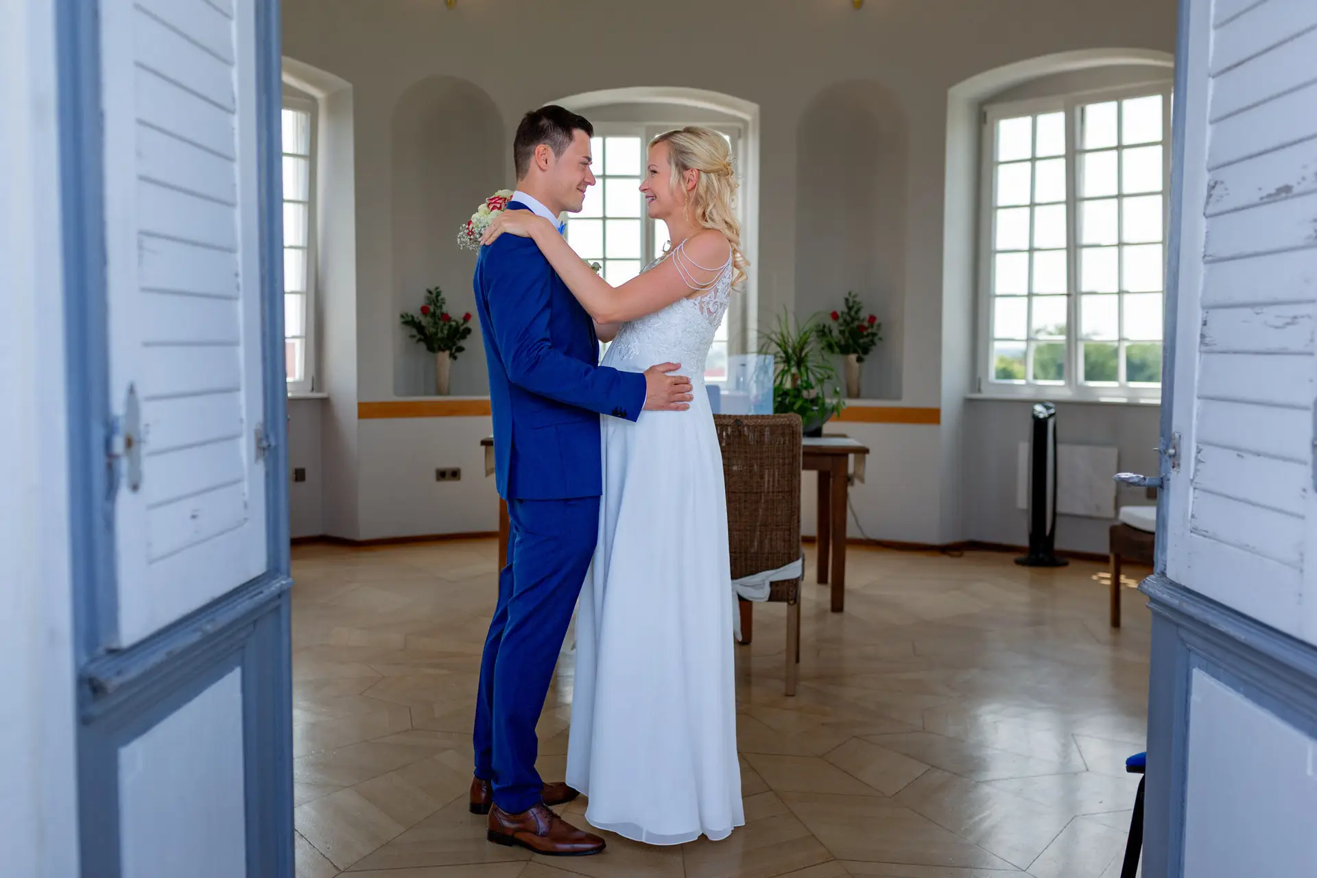 Liane und Kevin umarmen sich im Trausaal des Schlosspavillon, Blick durch die offene Flügeltür