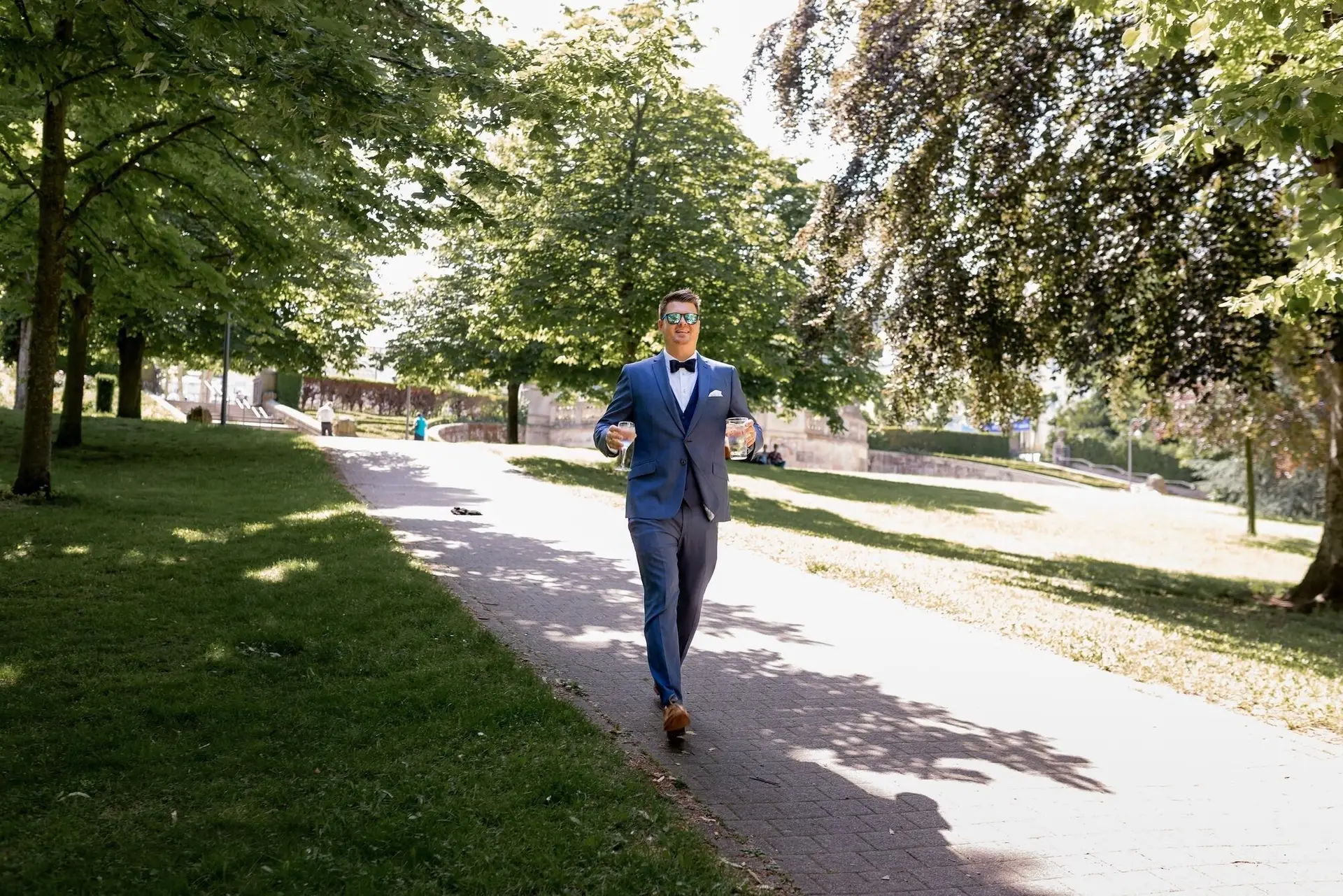 Tina Bjoern Kurpark Braeutigam Sonnenbrille Glaeser.1k8udFW7 Bräutigam im dunkelblauen Anzug und Sonnenbrille bringt zwei Gläser durch den Kurpark Bad Dürkheim