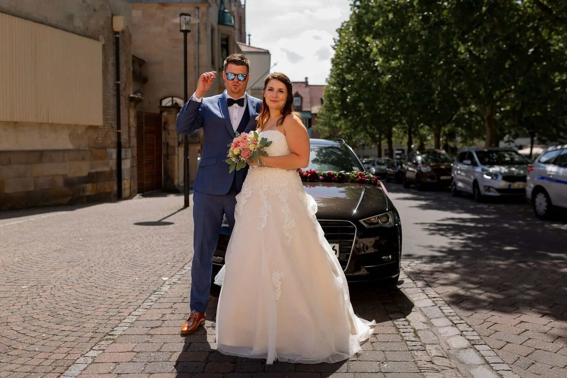 Tina Bjoern Mutterstadt Hochzeitsauto Pflasterstrasse.C1tcw6m5 Brautpaar vor schwarzem Hochzeitsauto auf gepflasterter Straße nach der Trauung in Mutterstadt