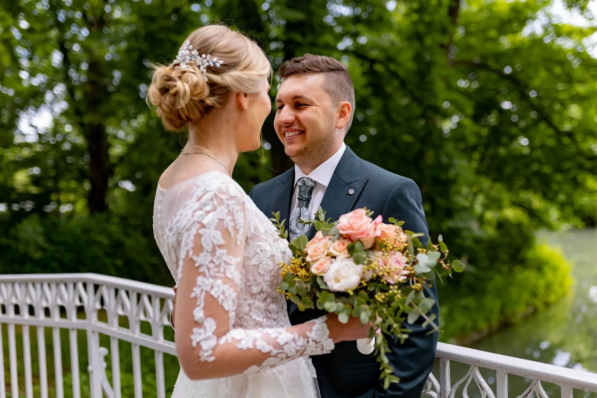 Brautpaar steht sich auf der weißen Brücke über dem Schlosspark-Bach gegenüber, Braut mit floralem Haarschmuck
