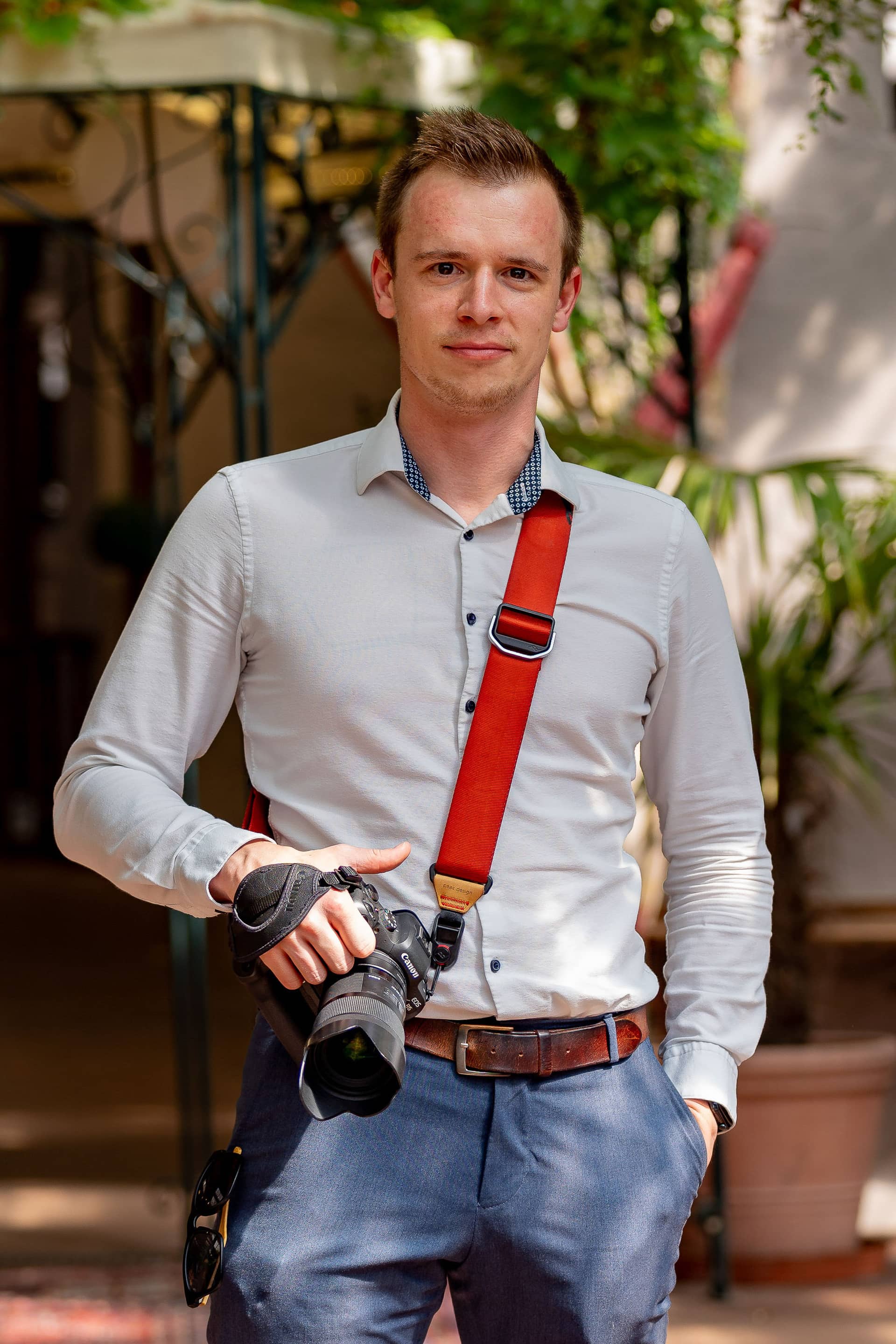 Hochzeitsfotograf in Deidesheim: Portrait eines Fotografen mit Kamera und rotem Kameragurt, aufgenommen im Grünen als professionelles Profilbild für Hochzeiten.