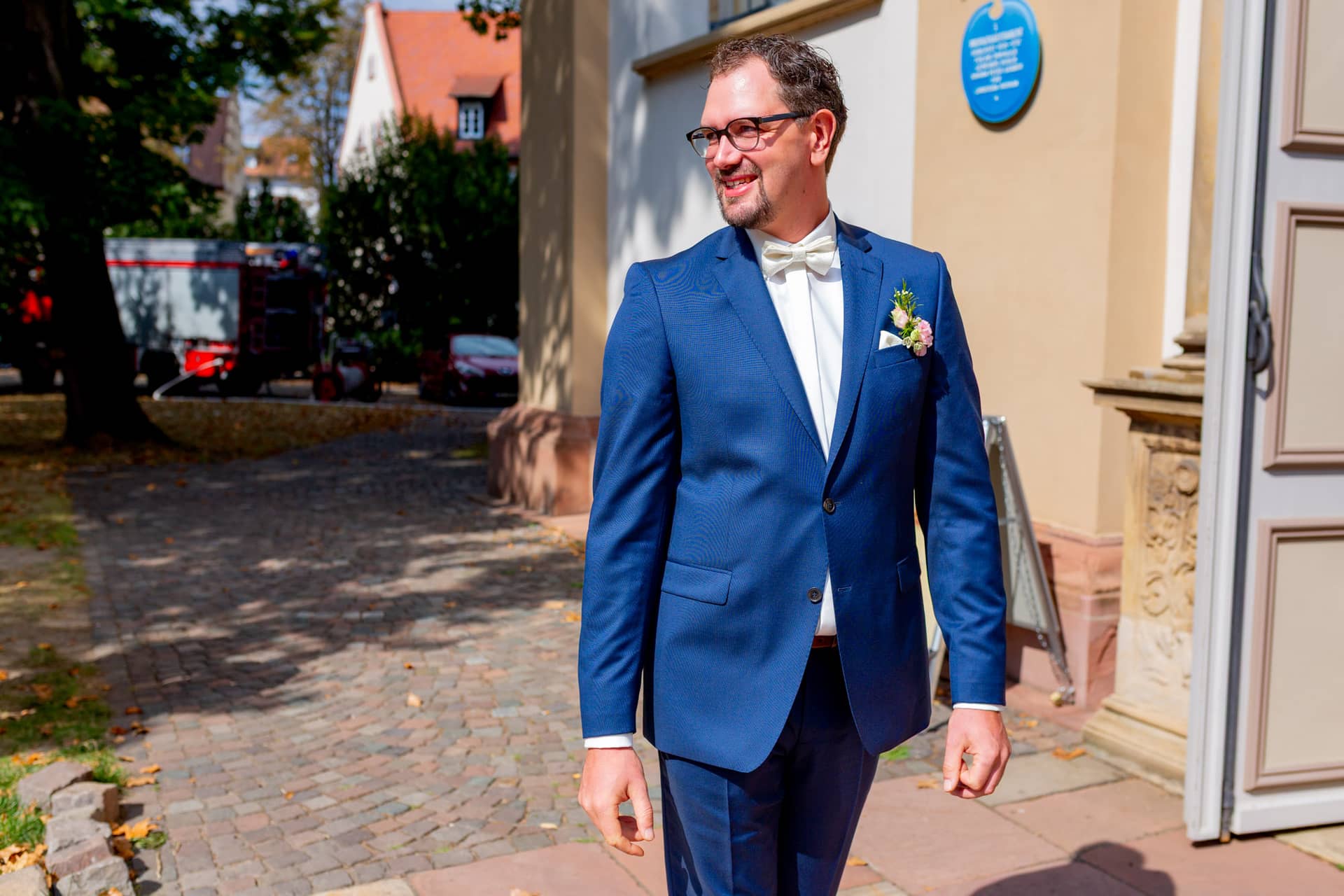 20180915 13 29 57 MK3 4876 Brautpaar Hochzeit Anzug Blume Hochzeitsfotograf Reilingen Speyer Ida Philipp.BPnpAE24 Brautpaar im eleganten Marineblau vor dem Kirchenportal bei sonnigem Wetter