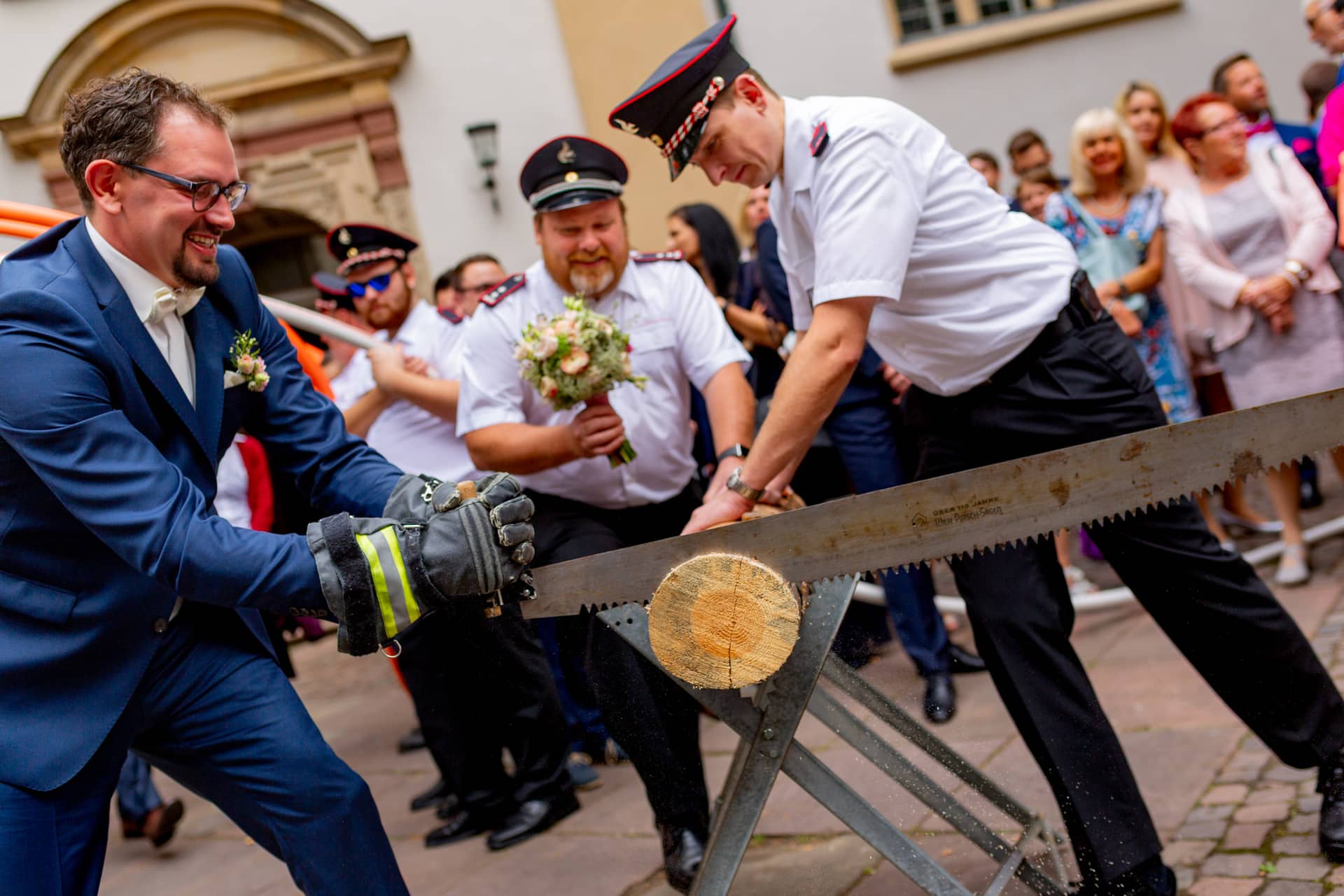 20180915 14 30 08 MK3 5529 Hochzeit Feuerwehr Maenner Saege Hochzeitsfotograf Reilingen Speyer Ida Philipp.CiVe1buX Brautpaar schafft gemeinsam den Holzstamm beim Baumstammsägen vor der Kirche