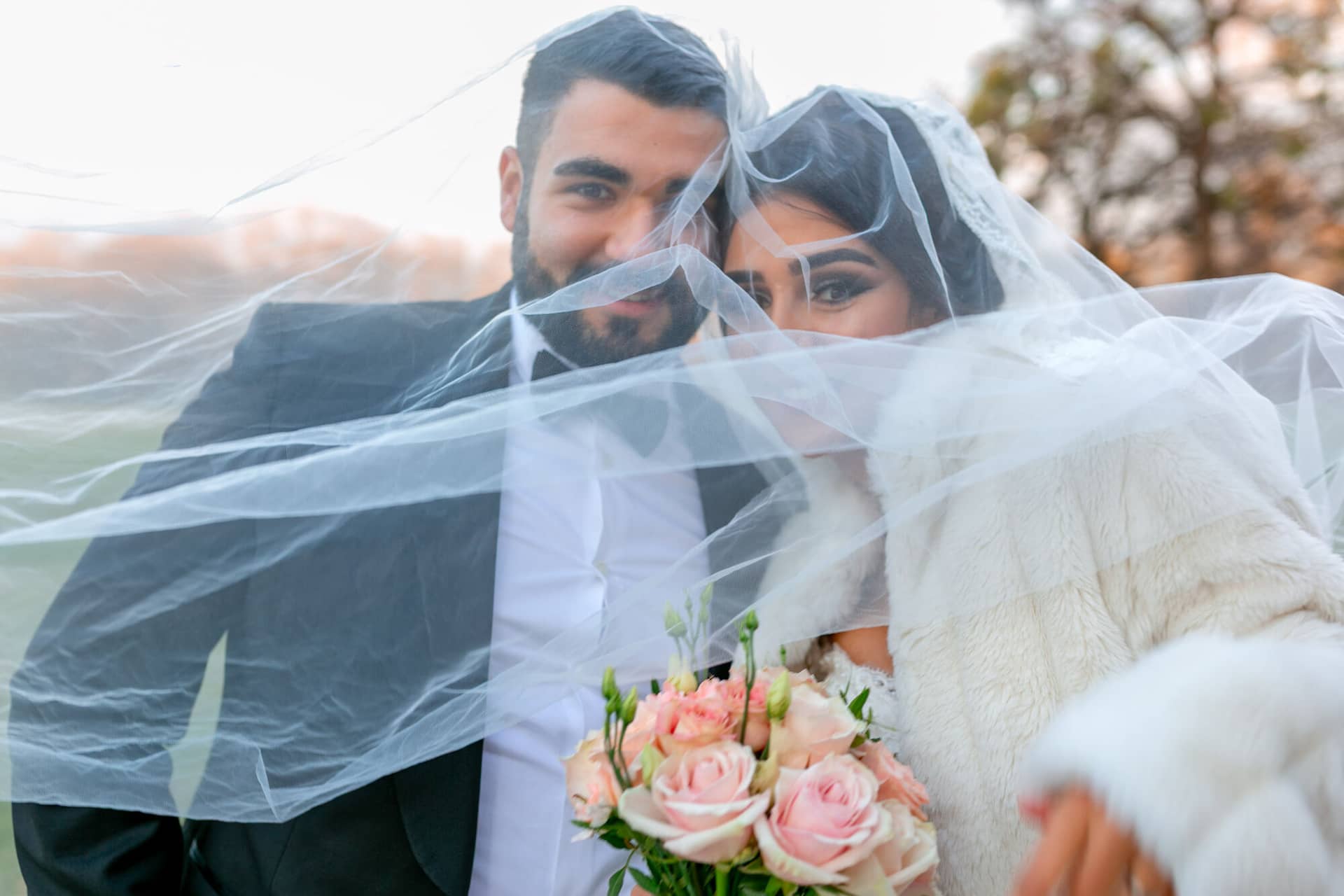 20181225 16 49 20 MK3 4512 Brautpaarshooting Worms Hochzeitsfeier Mannheim.Ds992OV2 Brautpaar umschlingt sich innig unter weißem Schleier, rosa Blumenstrauß und kahle Äste im winterlichen Schlossgarten Worms-Herrnsheim