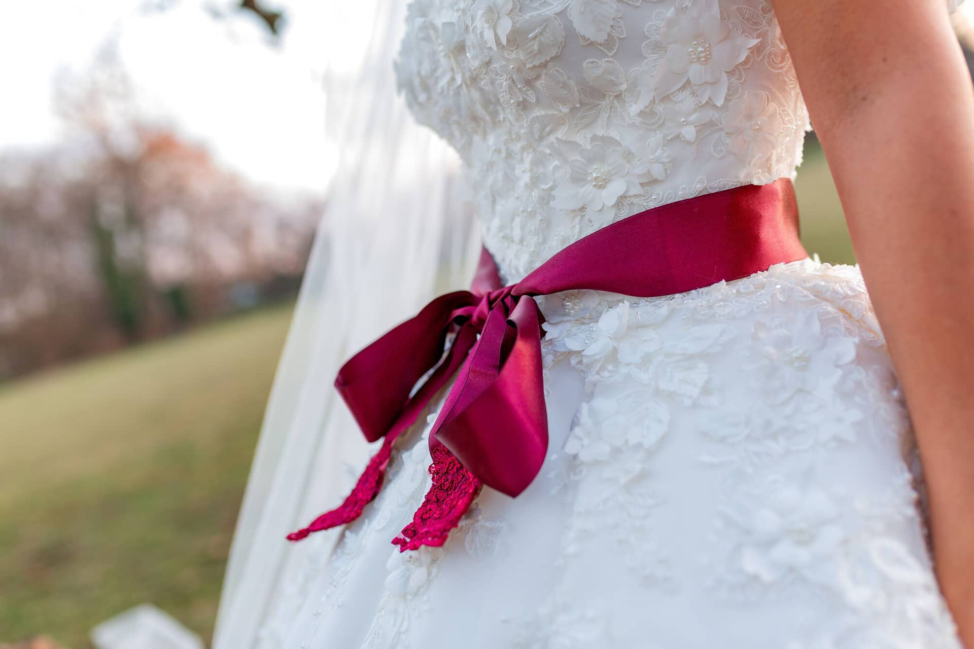 20181225 17 19 48 MK3 4719 Brautpaarshooting Worms Hochzeitsfeier Mannheim.OFXaikYz Nahaufnahme des floralen Hochzeitskleides der Braut mit tiefrotem Satinband, zarter Spitzenstoff im Detail