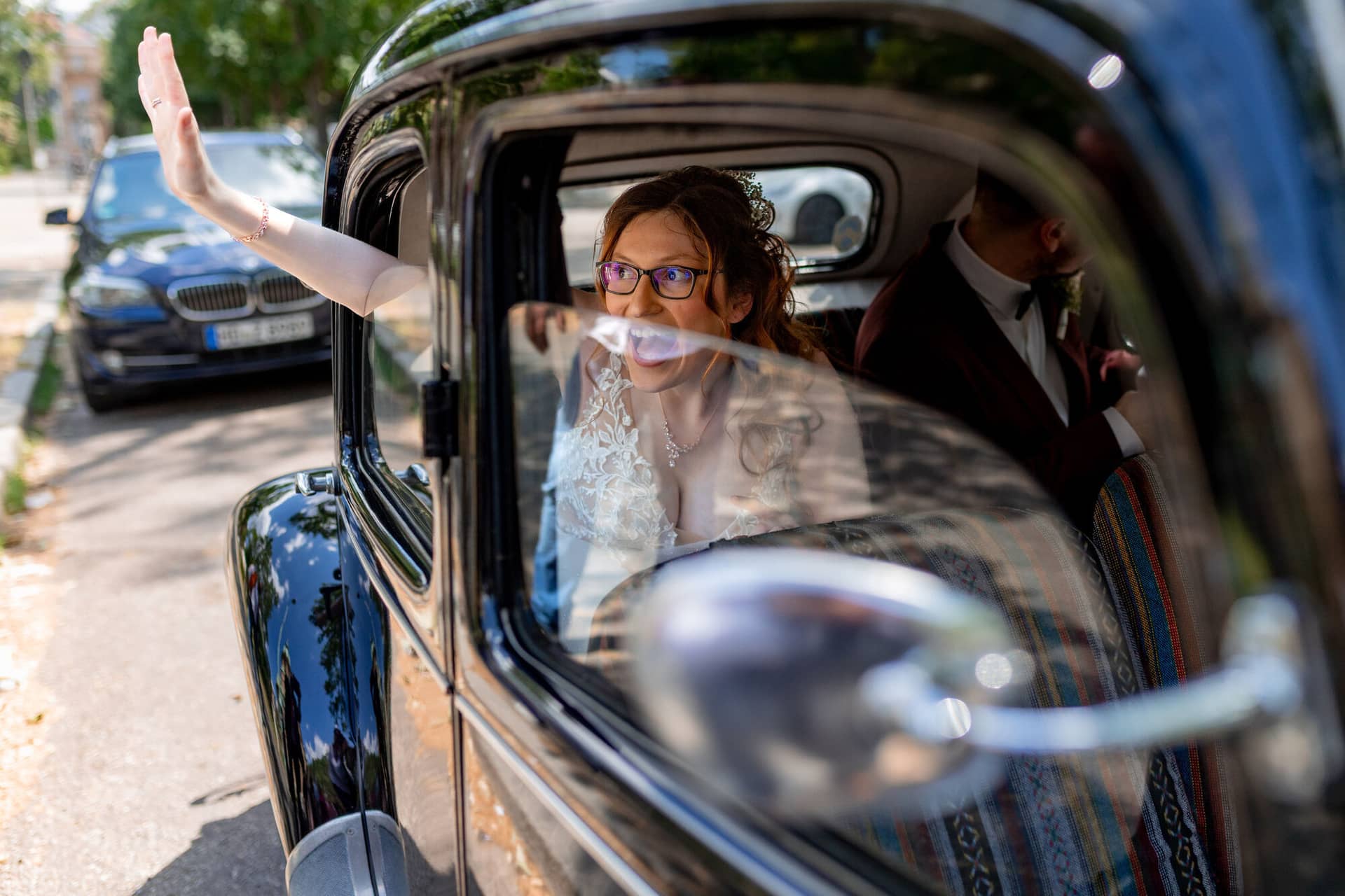 20230610 14 09 38 4K8A1283 Hochzeitsfotograf Mannheim Christuskirche Neuleiningen Burgschenke.VD NOleN Braut mit Brille und Schleier sitzt strahlend in einem alten Citroën, Bräutigam im Hintergrund