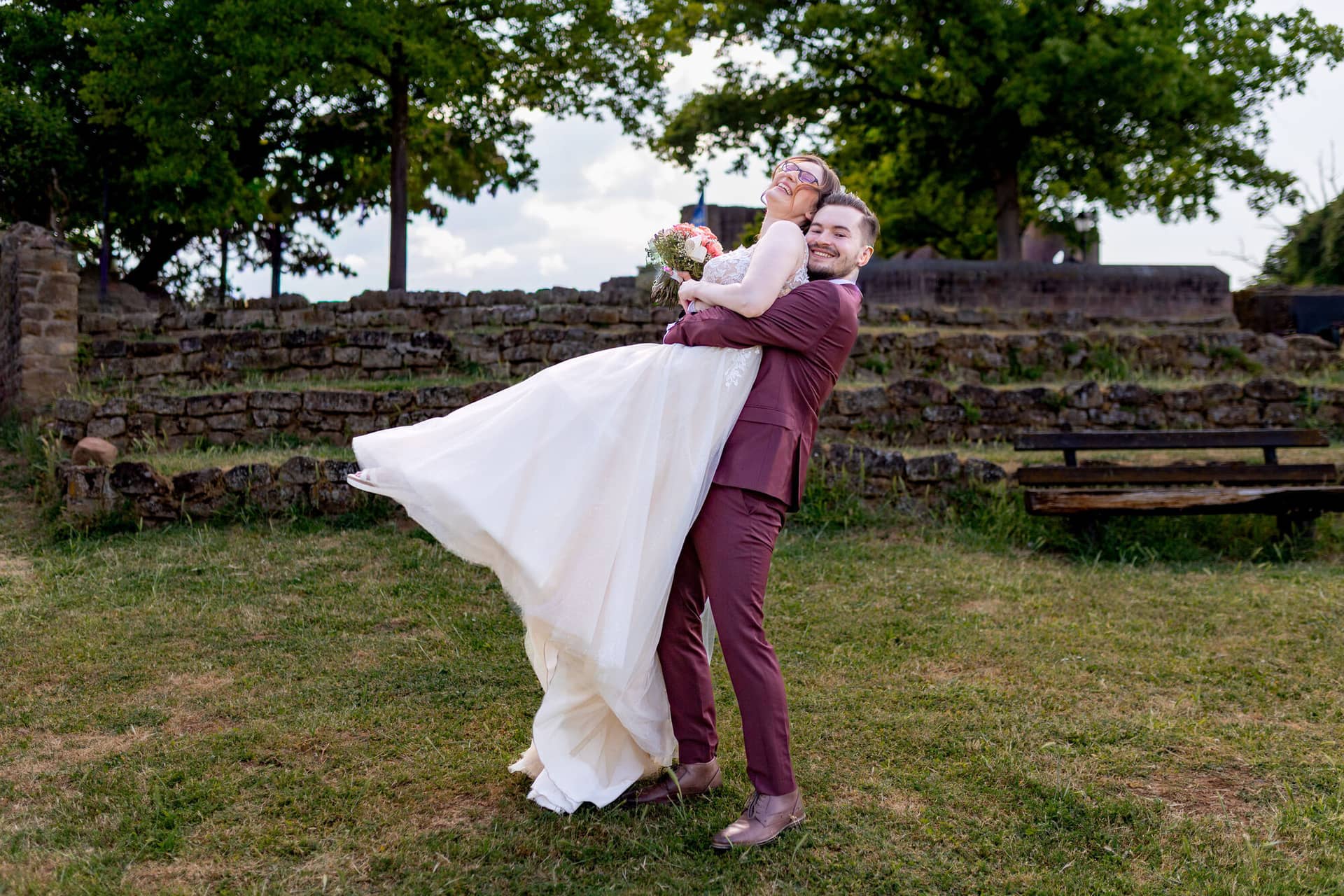 20230610 17 56 54 4K8A3882 Hochzeitsfotograf Mannheim Christuskirche Neuleiningen Burgschenke.Dhowvczh Bräutigam hebt seine Braut schwungvoll in die Luft vor der Bruchsteinmauer der Burg Neuleiningen