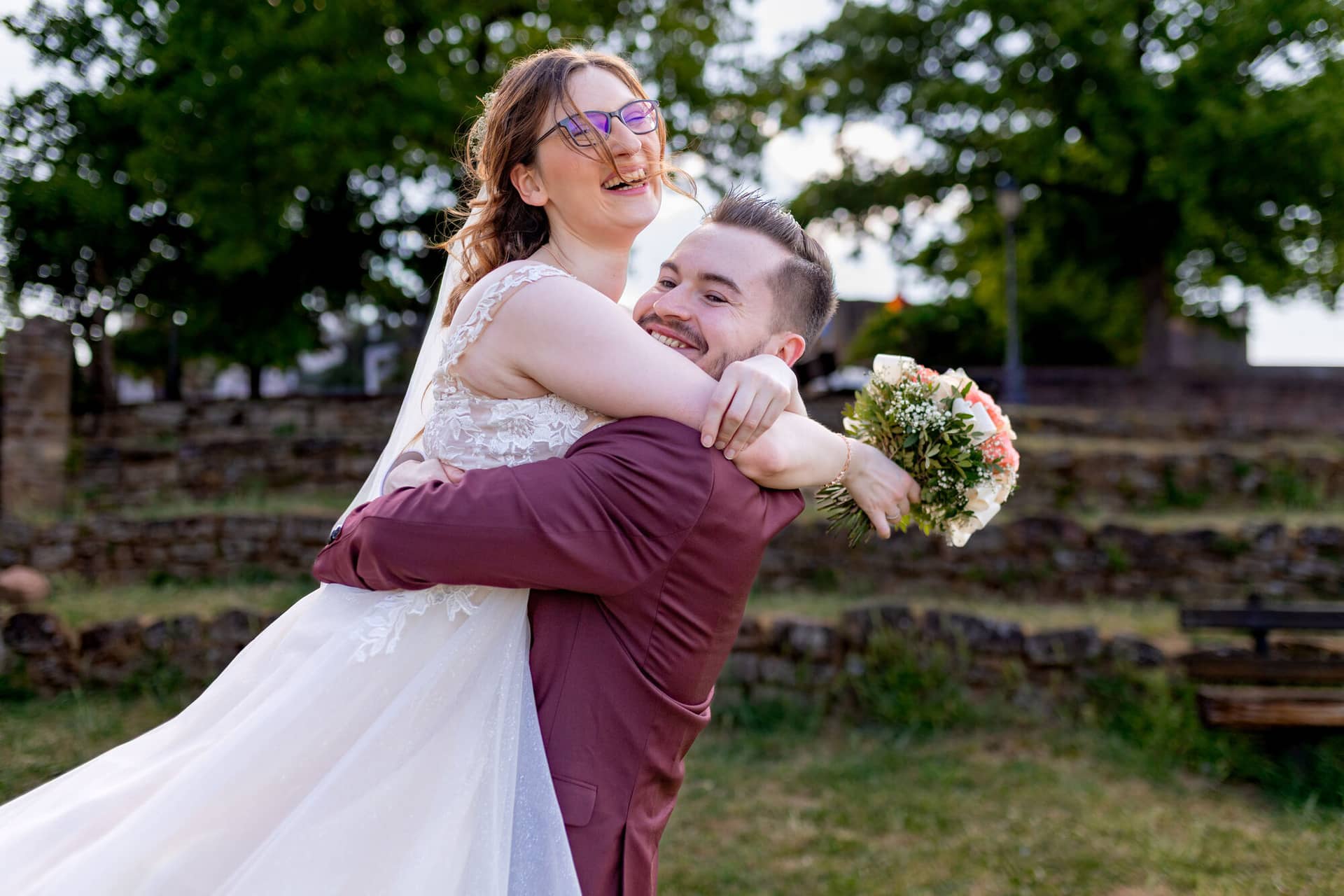 20230610 17 57 07 4K8A3941 Hochzeitsfotograf Mannheim Christuskirche Neuleiningen Burgschenke.BgOwEoVR Bräutigam trägt seine lachende Braut ausgelassen hoch vor der Bruchsteinmauer der Burgschenke