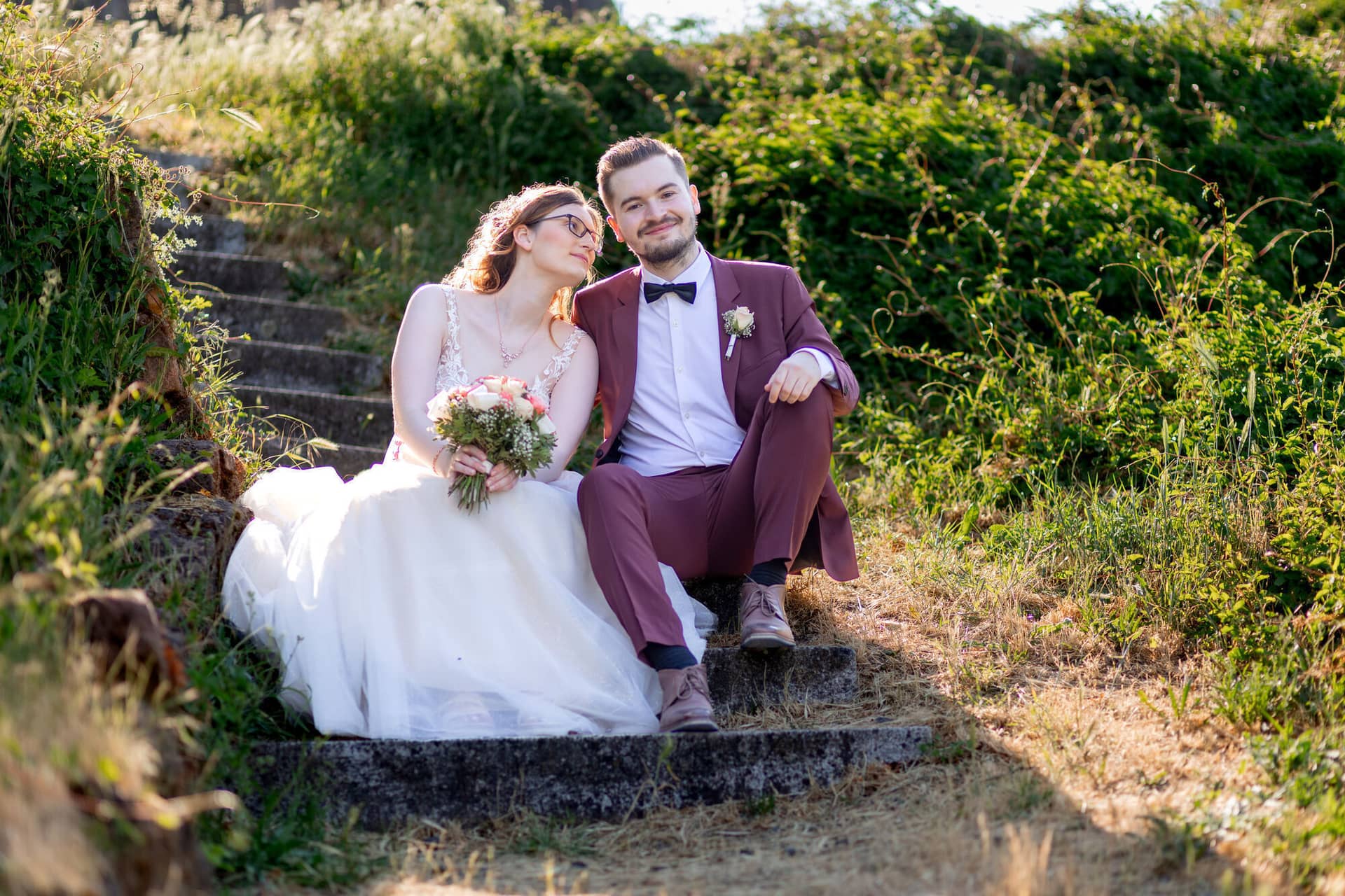 20230610 18 12 34 4K8A4303 Hochzeitsfotograf Mannheim Christuskirche Neuleiningen Burgschenke.BeyA1kcI Brautpaar sitzt auf einer alten Steintreppe der Burganlage und schaut sich liebevoll an, umgeben von Grün