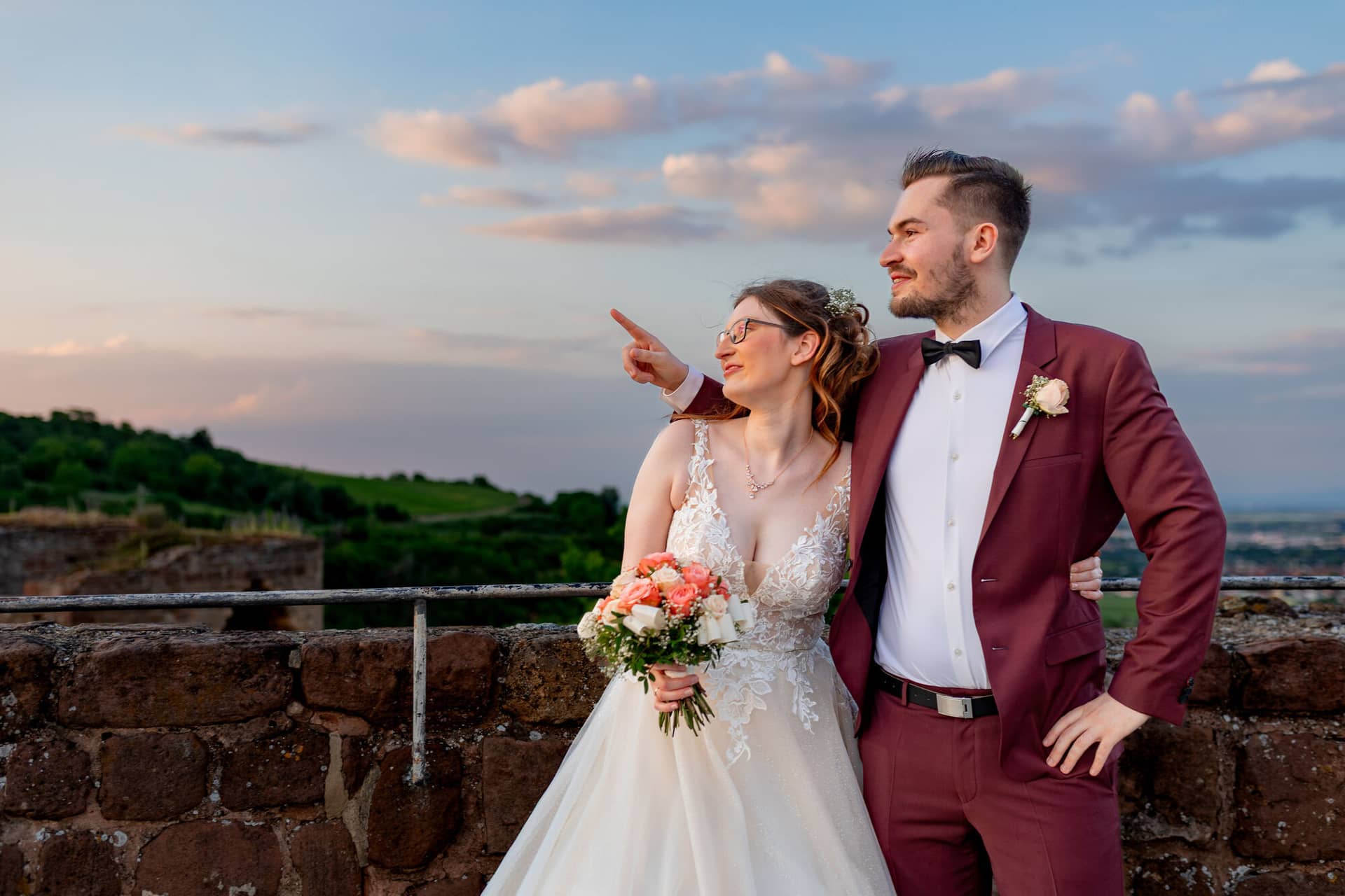 20230610 21 07 16 4K8A6517 Hochzeitsfotograf Mannheim Christuskirche Neuleiningen Burgschenke.BVMb14uS Brautpaar lacht herzlich und deutet auf den Horizont bei dramatischem Sonnenuntergang über der Burg Neuleiningen