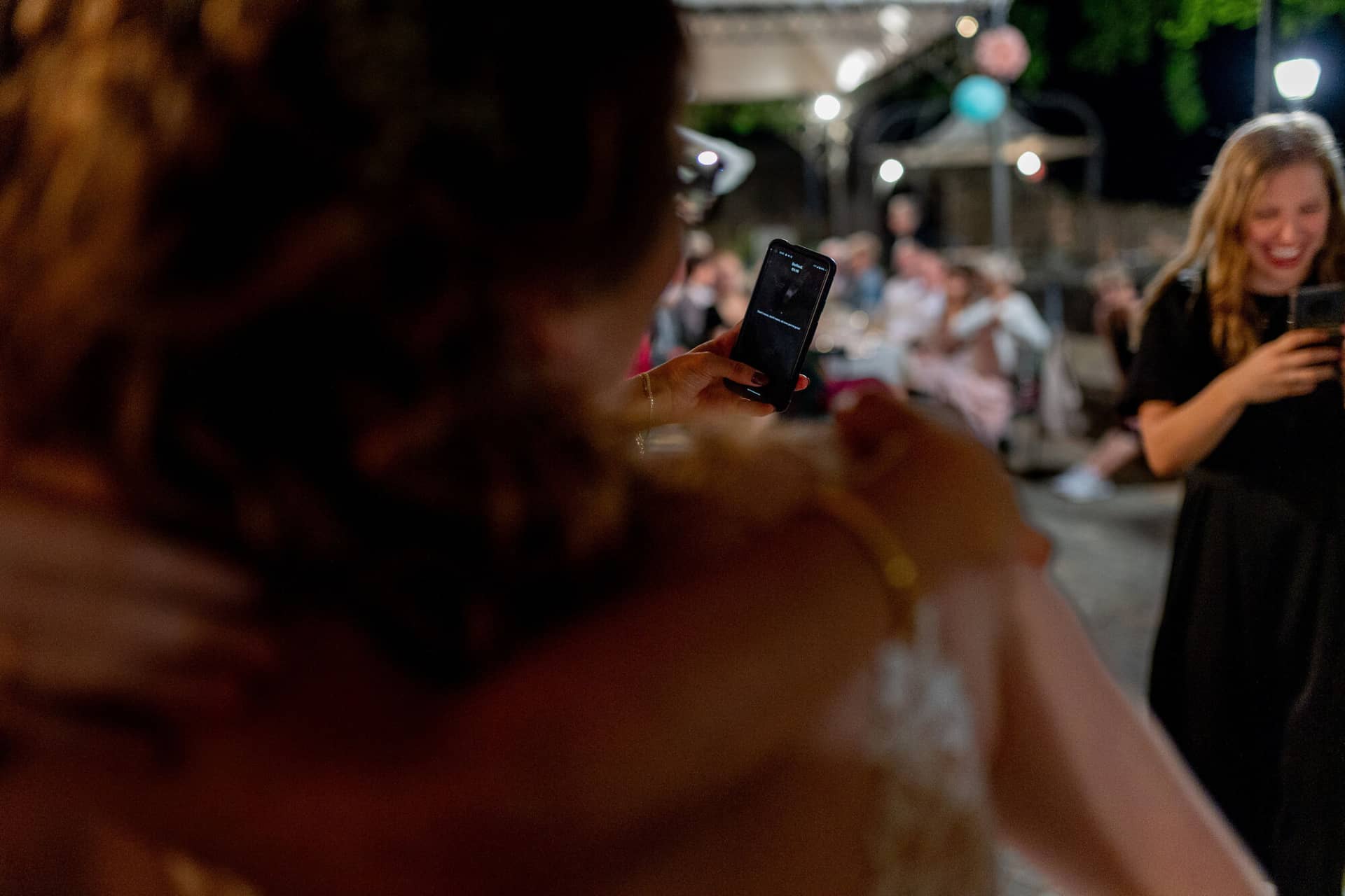 20230610 23 24 59 4K8A8746 Hochzeitsfotograf Mannheim Christuskirche Neuleiningen Burgschenke.BUFCzi5b Braut hält Smartphone hoch und fotografiert feiernde Gäste in der Dämmerung bei der Hochzeitsparty