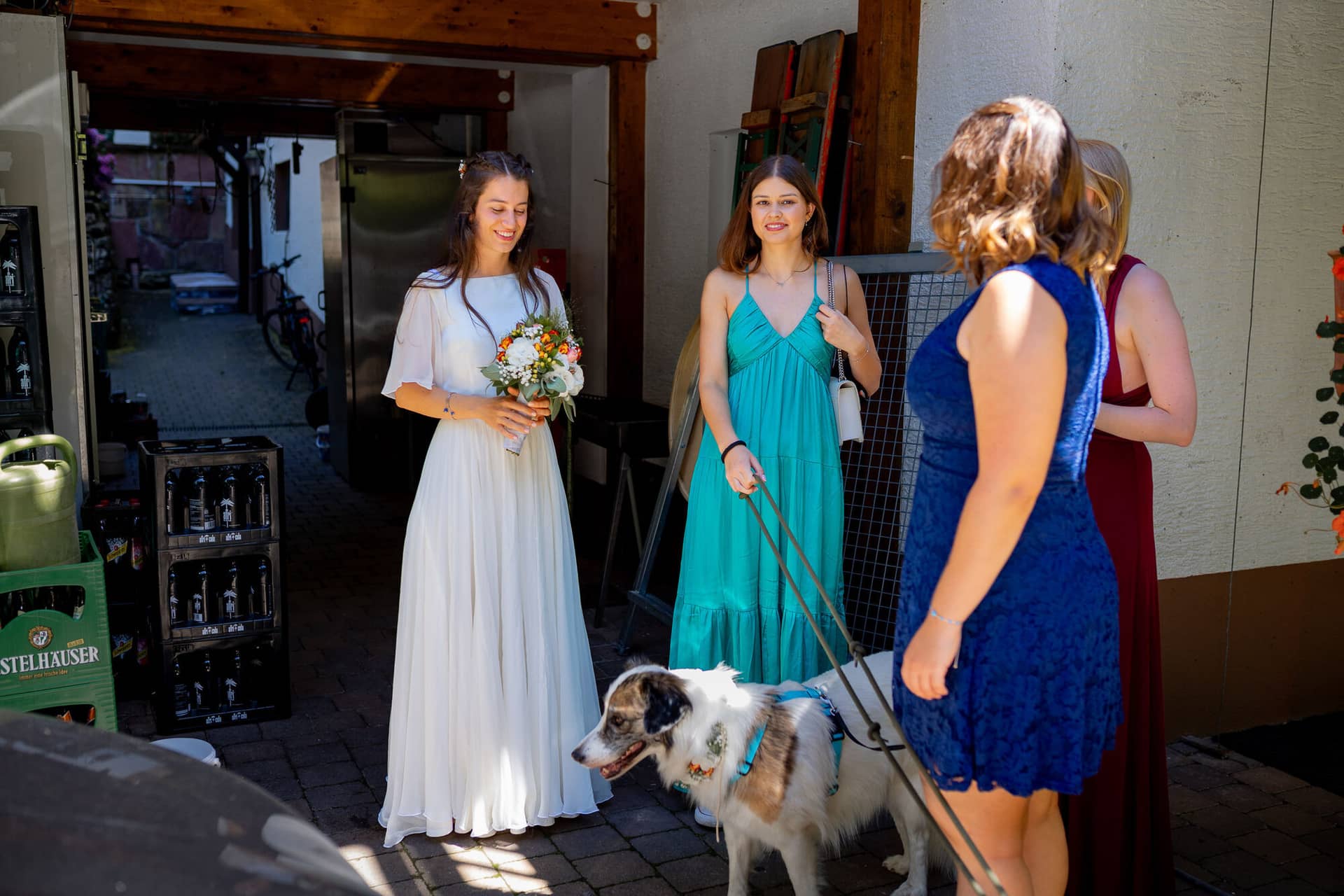 20230811 14 23 35 Hochzeit Elztal Hochzeitsfotograf Heiraten Heidelberg Landgasthof Heidersbacher Muehle 4K8A0793.CcIfZpe0 Braut mit Brautjungfern und Familienhund vor dem historischen roten Holzhaus der Heidersbacher Mühle