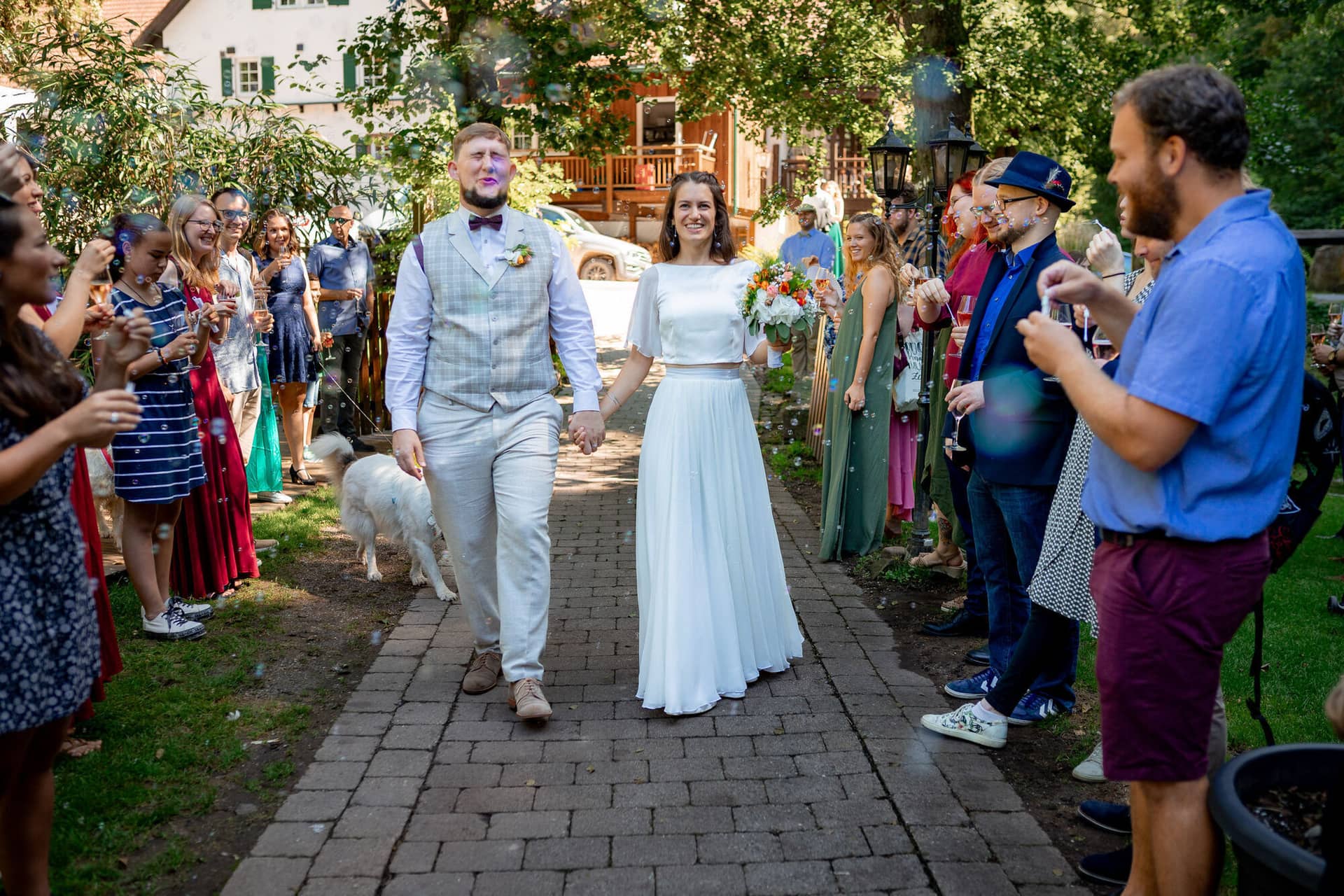 20230811 15 35 43 Hochzeit Elztal Hochzeitsfotograf Heiraten Heidelberg Landgasthof Heidersbacher Muehle 4K8A4649. B72ab9f Brautpaar schreitet Arm in Arm durch die jubelnden Gäste mit Seifenblasen, Sommer-Atmosphäre pur