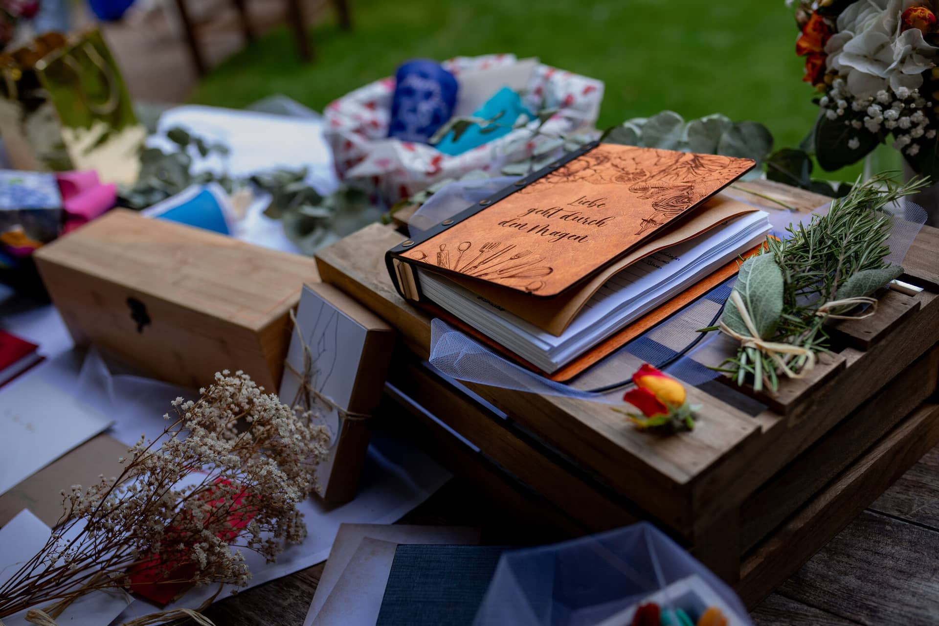 20230811 16 21 34 Hochzeit Elztal Hochzeitsfotograf Heiraten Heidelberg Landgasthof Heidersbacher Muehle 4K8A5220 Verbessert RR.DAtUv75w Detailaufnahme der Hochzeitsdekoration – Notizbuch, Scheren und Blumen auf dem Rasen als Deko-Element