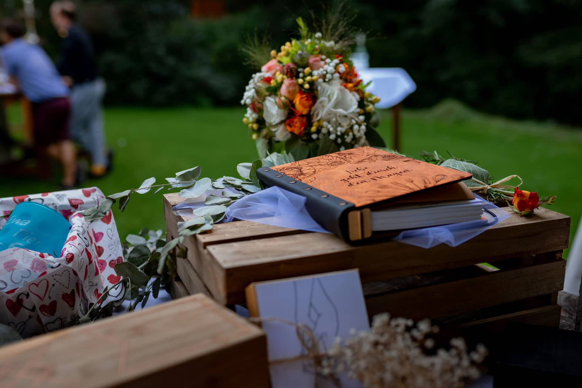 20230811 16 21 52 Hochzeit Elztal Hochzeitsfotograf Heiraten Heidelberg Landgasthof Heidersbacher Muehle 4K8A5246 Verbessert RR.CGR5vVI7 Rustikales Holzbord mit persönlichem Gästebuch und Blumenkrone als Deko-Arrangement