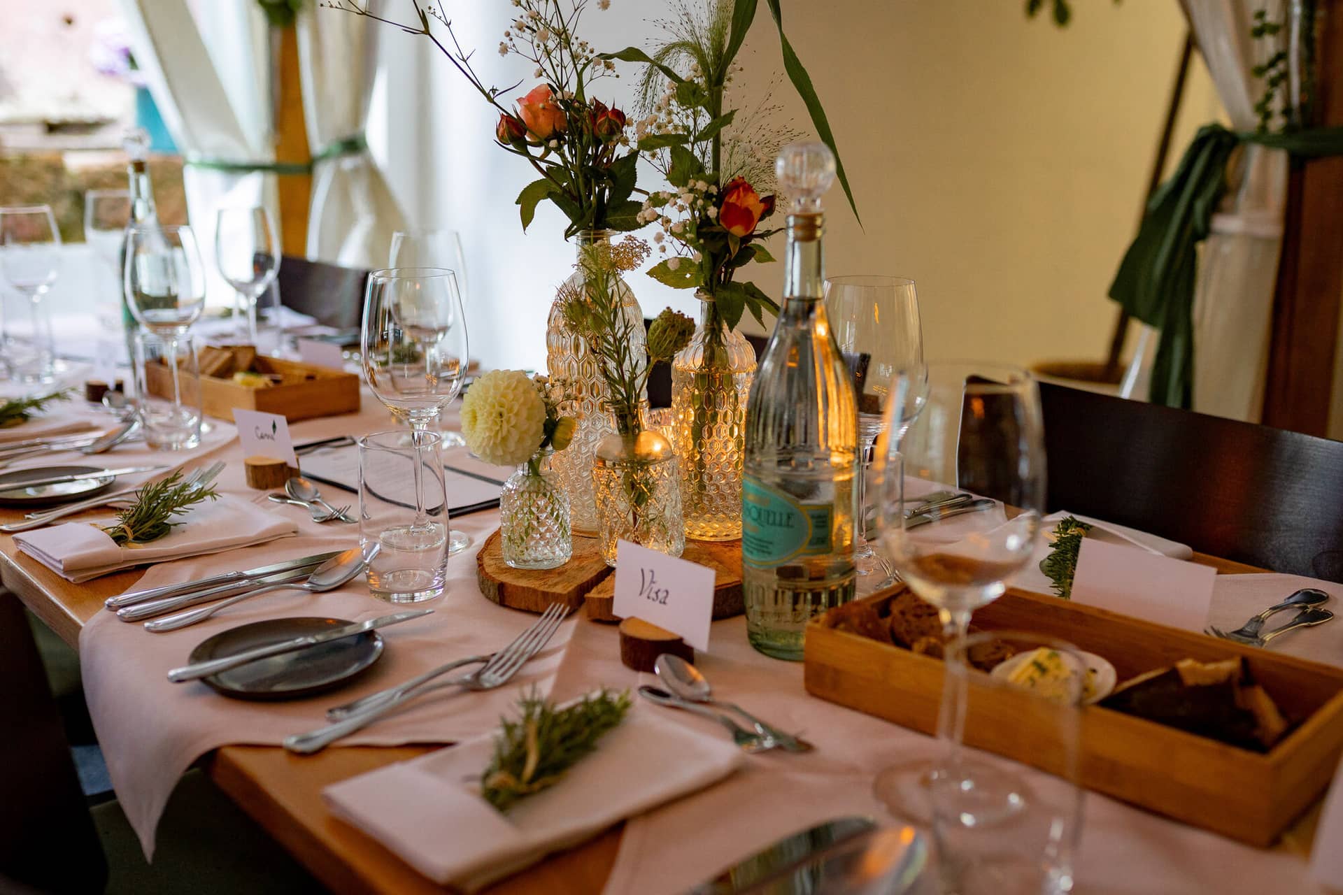 20230811 18 39 45 Hochzeit Elztal Hochzeitsfotograf Heiraten Heidelberg Landgasthof Heidersbacher Muehle 4K8A7253.Bk Pgssq Langer Festtisch mit hellrosa Tischdecken und Holzscheiben, Gäste versammeln sich zum Abendessen