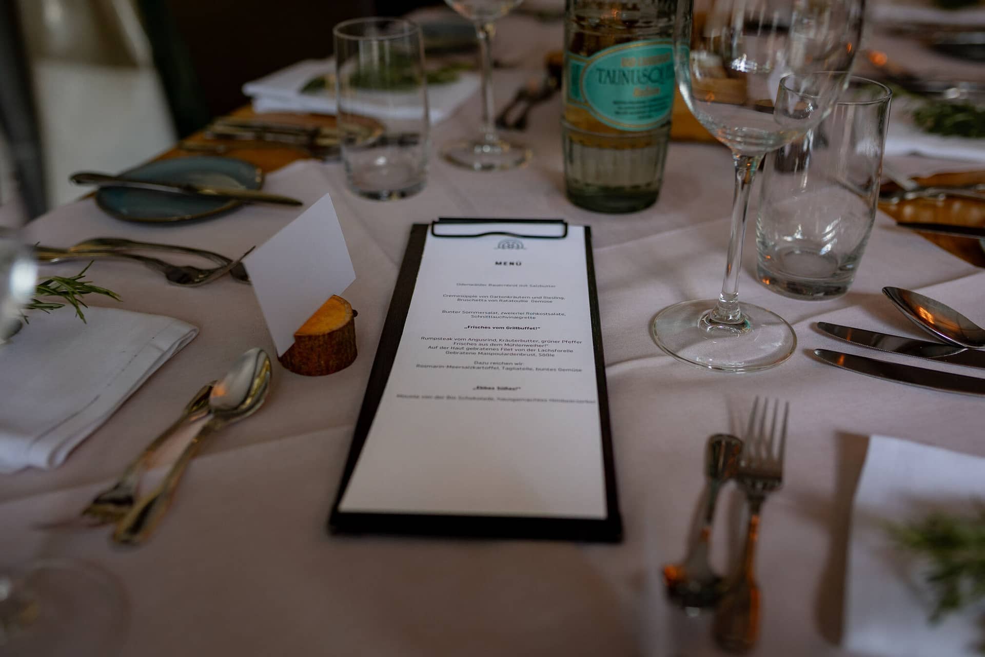 20230811 18 40 11 Hochzeit Elztal Hochzeitsfotograf Heiraten Heidelberg Landgasthof Heidersbacher Muehle 4K8A7260.DZ3E4r5x Tischdetail des Hochzeitsabendessens: Menükarte, Weinflasche und persönliche Dekoration