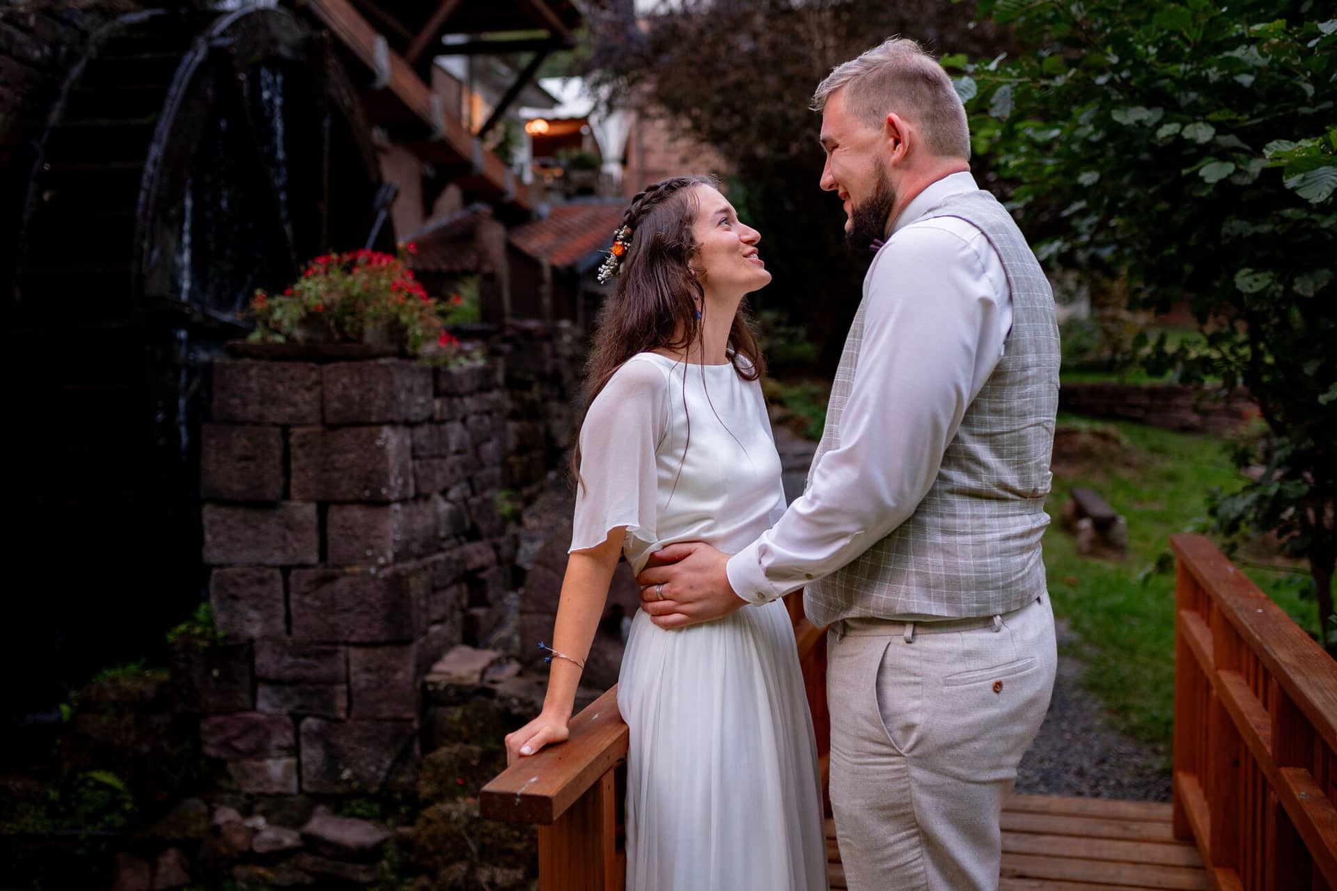20230811 20 42 56 Hochzeit Elztal Hochzeitsfotograf Heiraten Heidelberg Landgasthof Heidersbacher Muehle 4K8A7873.CjUKMS X Brautpaar küsst sich innig auf der Holzbrücke vor dem Wasserfall und der Steinmauer
