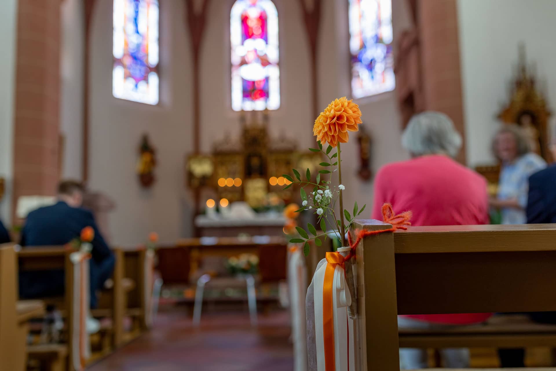 20240803 125235 4K8A3127.BPFauWTo Orangefarbene Blume in Glasvase dekoriert eine Kirchenbank in St. Johannes der Täufer Bad Münster