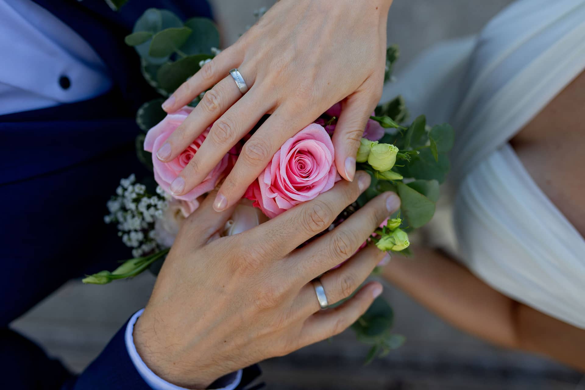 20240820 19 06 01 Teusch Schlossgarten Worms Herrnsheim 4K8A7458 Hochzeitsfotograf Matthias Butz.C8kwlK W Nahaufnahme der Hände des Brautpaares mit Ehering und einer rosa Rose