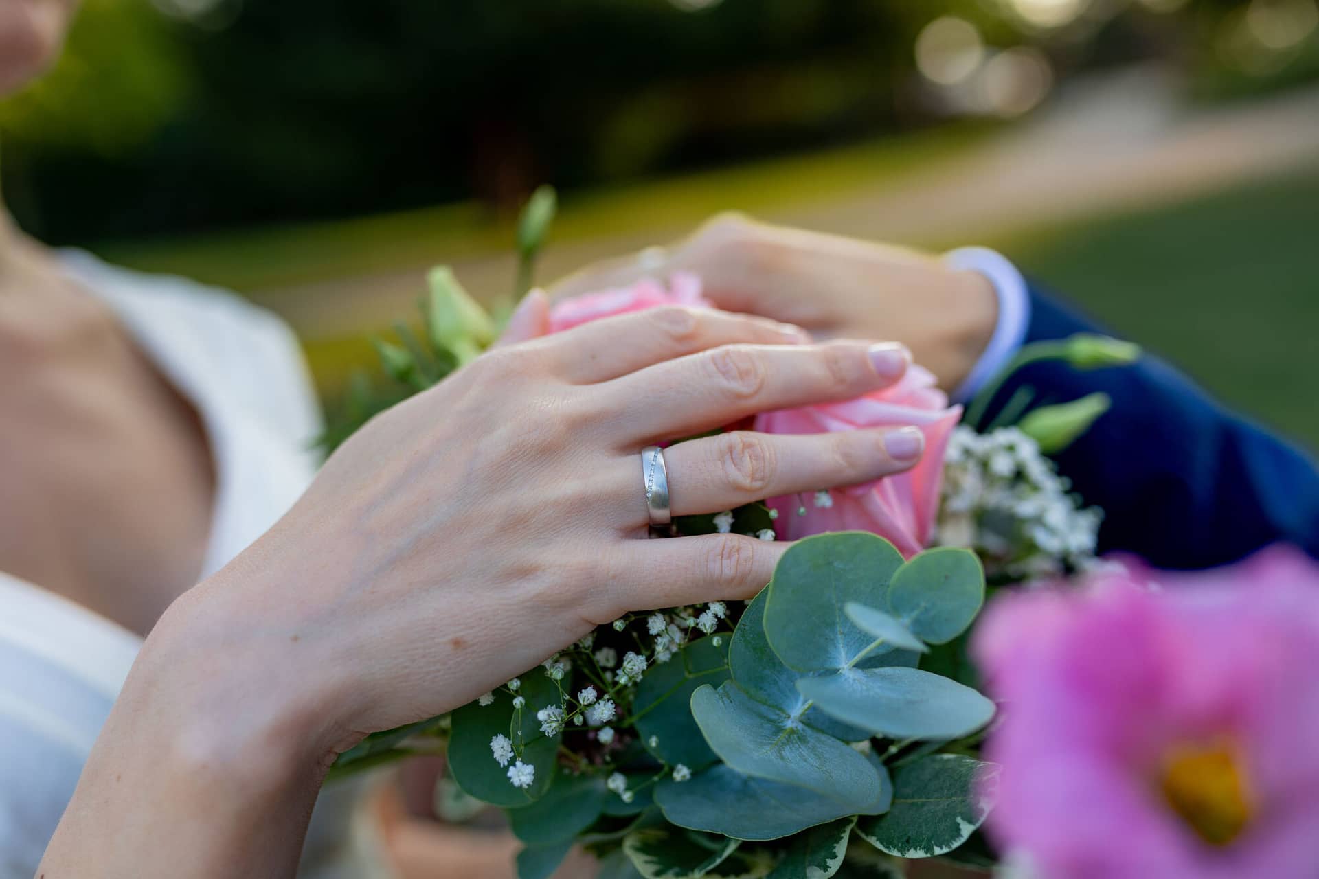 20240820 19 06 29 Teusch Schlossgarten Worms Herrnsheim 4K8A7491 Hochzeitsfotograf Matthias Butz.ChLuBaIX Braut hält Strauß aus rosa Rosen und Eukalyptus, Brautpaar hält sich an den Händen im Garten