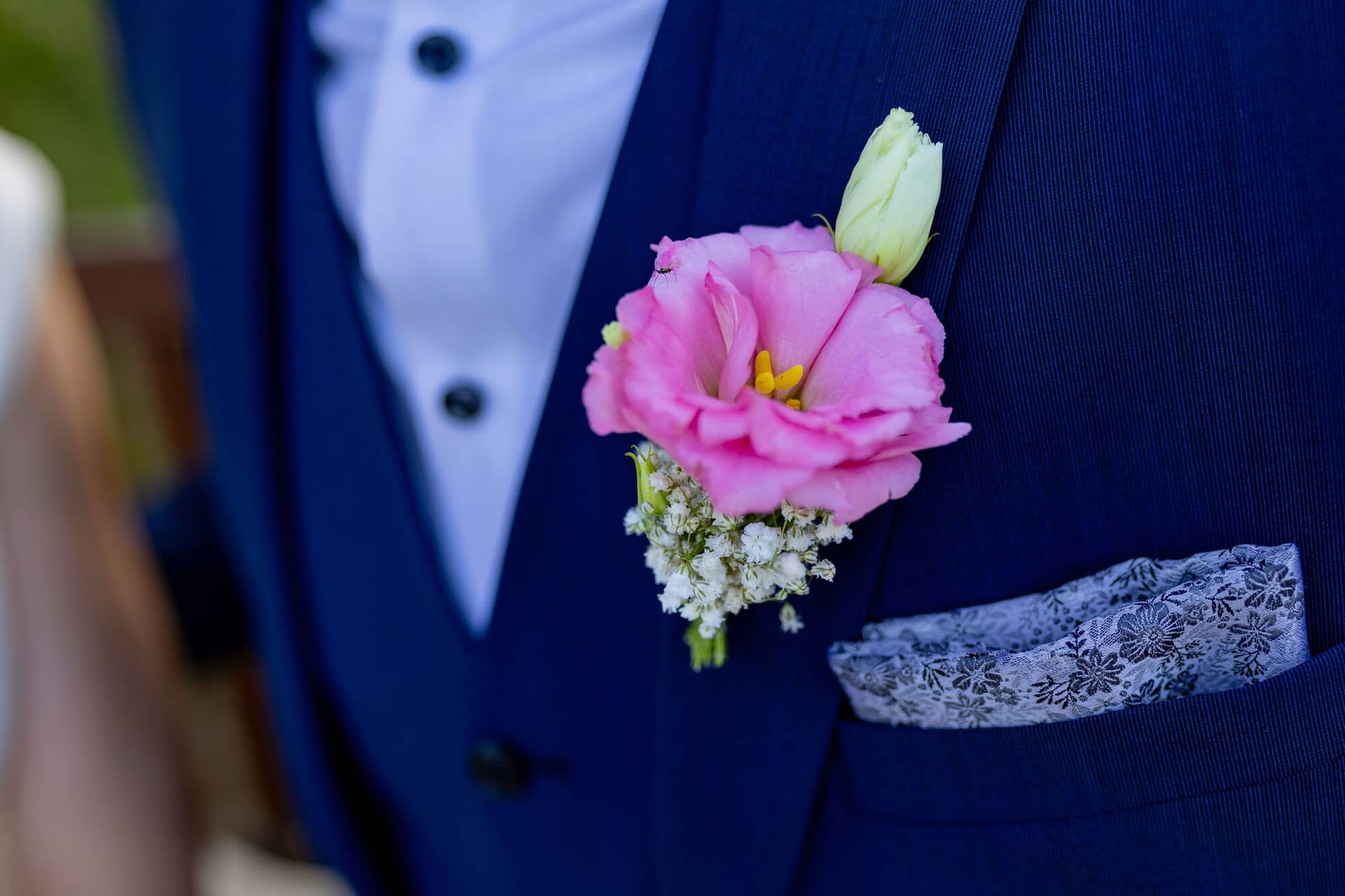 20240820 19 13 08 Teusch Schlossgarten Worms Herrnsheim 4K8A7646 Hochzeitsfotograf Matthias Butz.CeuBYuKk Nahaufnahme der Boutonnière aus rosa Lilie und weißen Blüten am Revers des Bräutigams im blauen Anzug