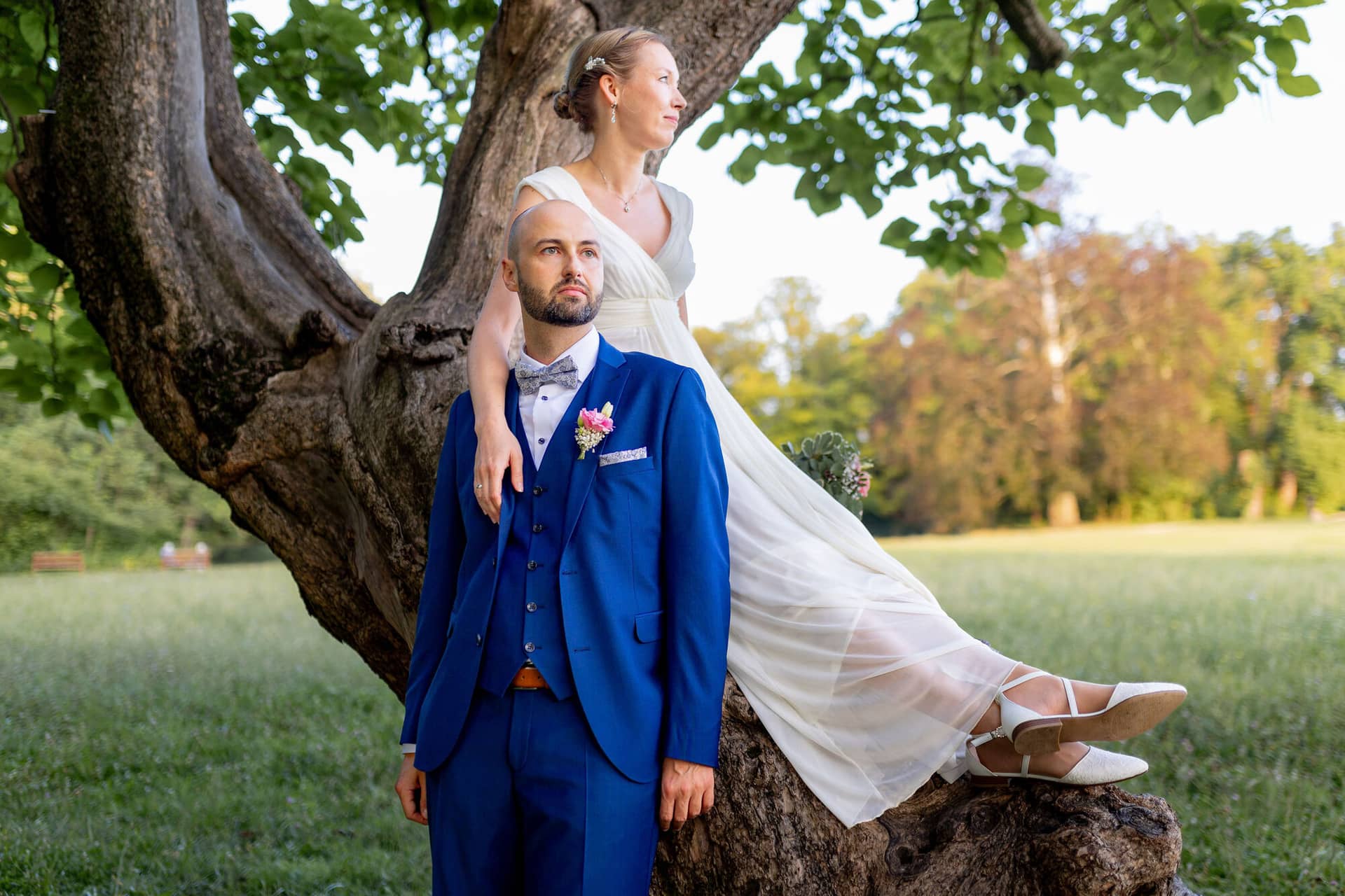 20240820 19 26 01 Teusch Schlossgarten Worms Herrnsheim 4K8A8227 Hochzeitsfotograf Matthias Butz.D DOVMZQ Brautpaar posiert unter einem großen alten Baum im Park, Braut hält den Schleier