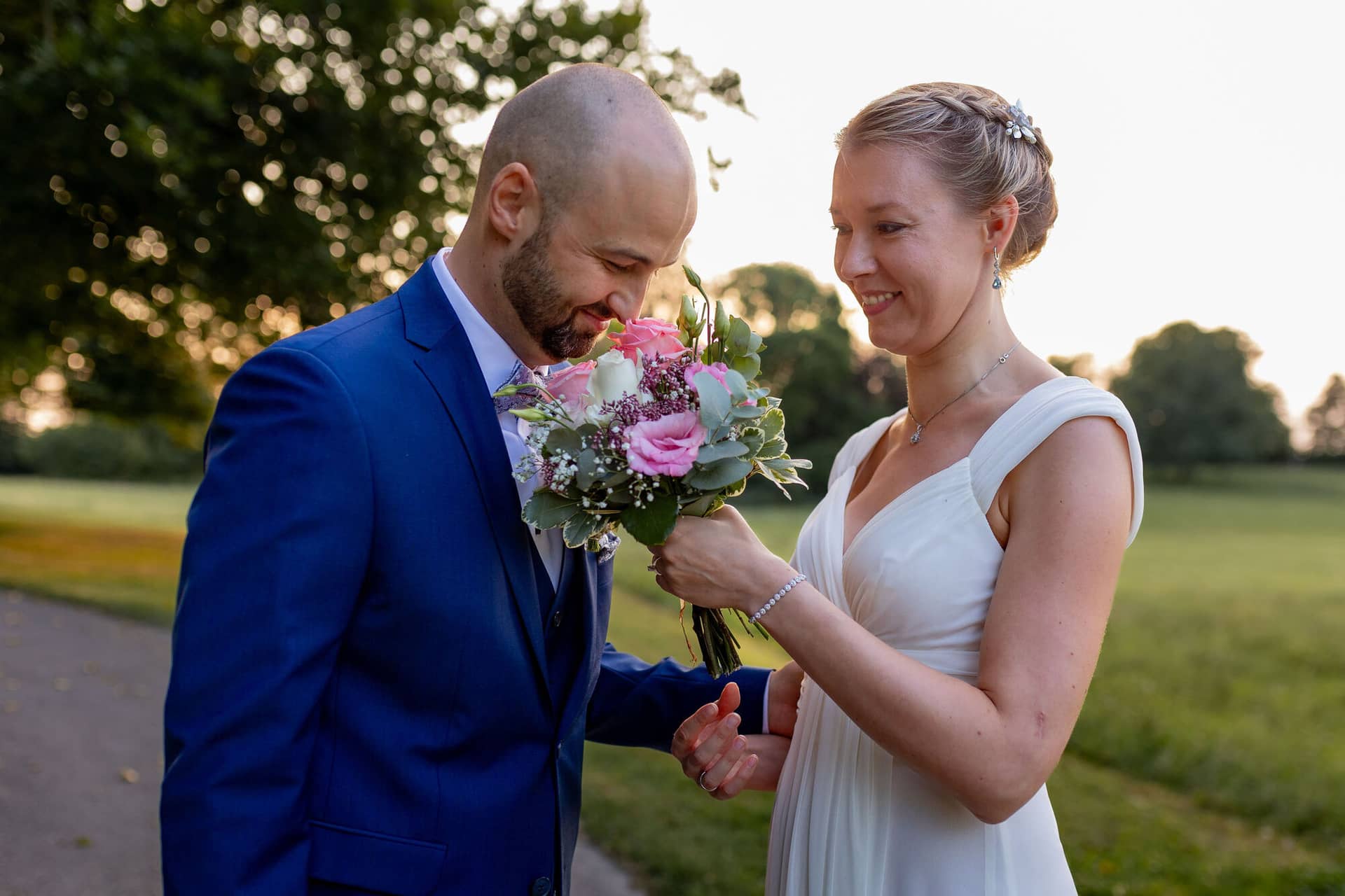 20240820 19 51 45 Teusch Schlossgarten Worms Herrnsheim 4K8A9369 Hochzeitsfotograf Matthias Butz.U CONF4D Braut zeigt dem Bräutigam den Ehering an ihrer Hand auf grüner Wiese