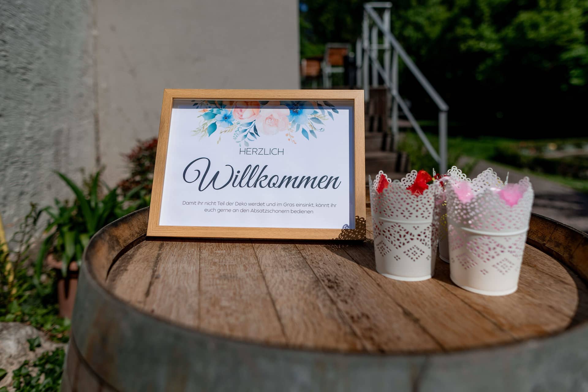 20250501 11 17 414K8A2293 Hochzeitslocation Bad Duerkheim Fritz Ritter Weingut.Dok Vhkq Herzlich Willkommen Schild mit Blumendeko auf rustikalem Weinfass