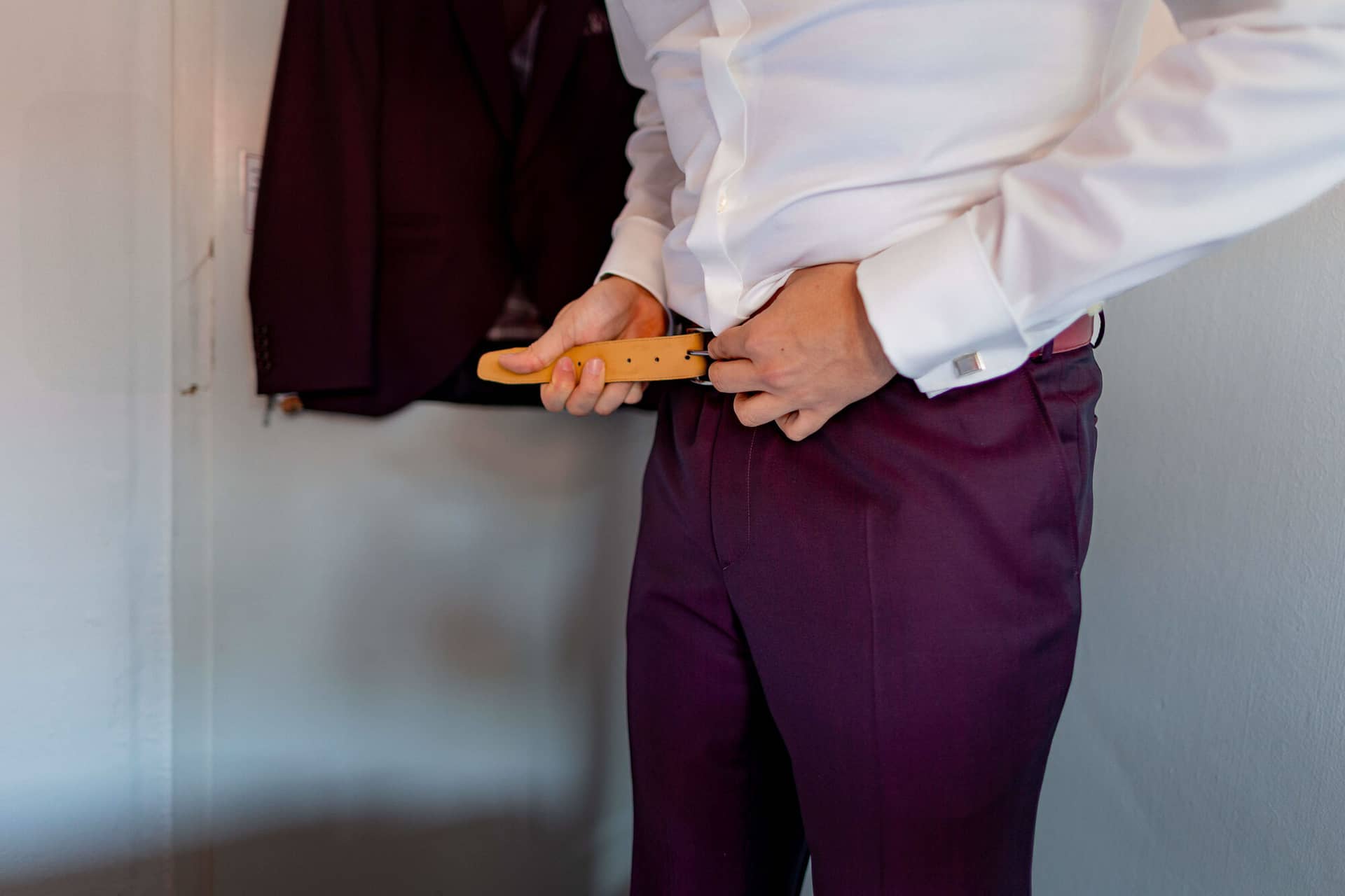20250501 11 31 404K8A2380 Getting Ready Brautigam Bad Duerkheim.CxQ4 F Bräutigam zieht braunen Ledergürtel zur bordeaux Anzughose an